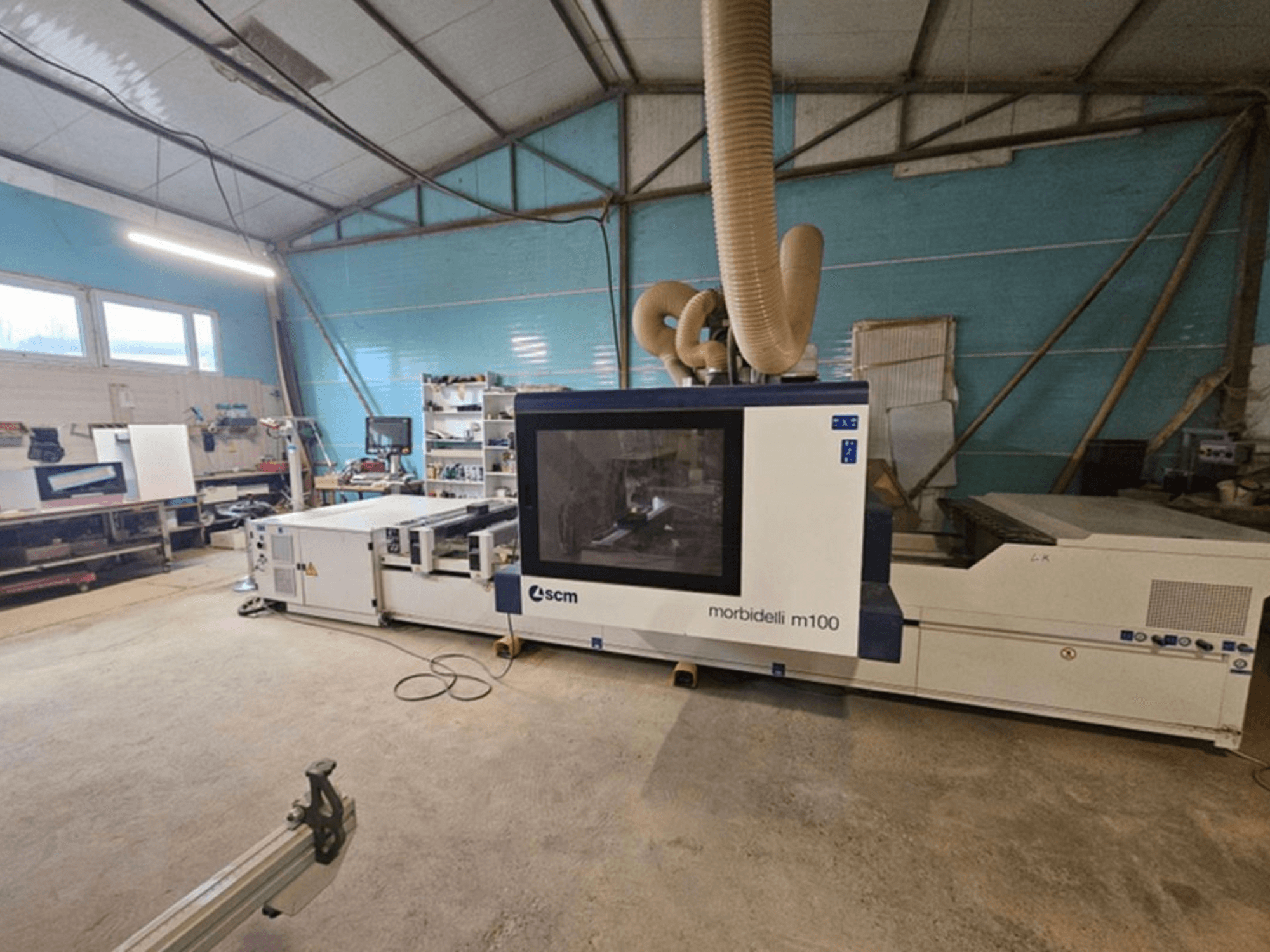 Centro de mecanizado CNC SCM MORBIDELLI M 100 en un taller, vista frontal con sistema de extracción de polvo y equipamiento del espacio de trabajo circundante.