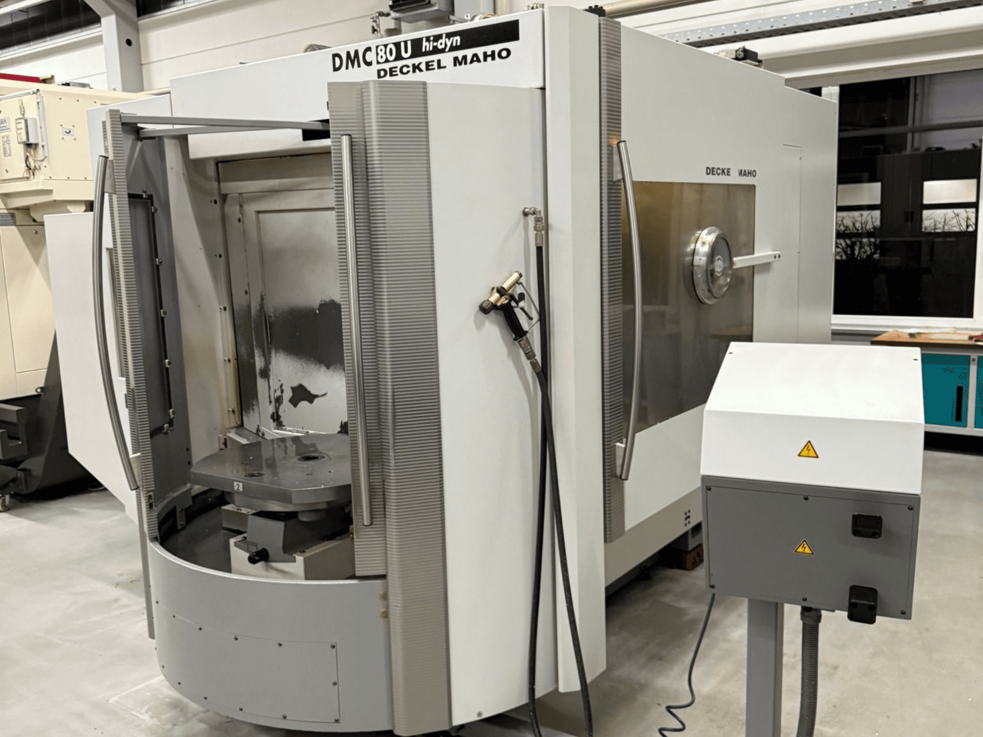 Vista frontal de una fresadora CNC de alta velocidad Deckel Maho DMC 80 U, con puerta de acceso abierta y panel de control en el lateral.