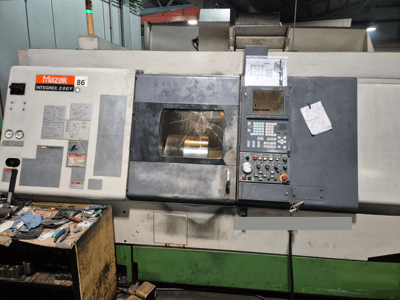 Máquina de torno Mazak Integrex 200Y, vista frontal, con panel de control y herramientas sobre un banco. Medidores visibles y pantalla de visualización.