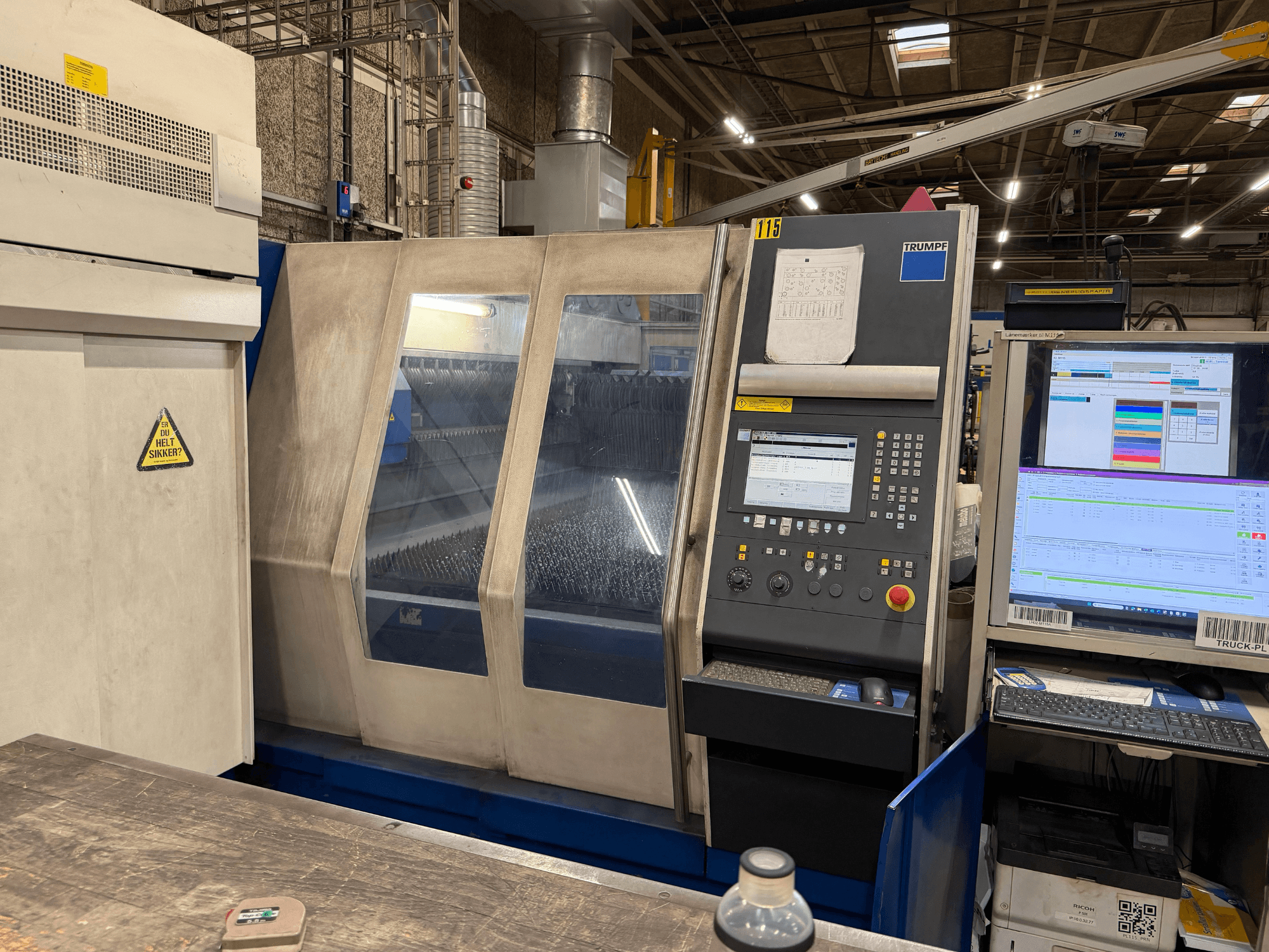 Vista frontal de una máquina láser industrial Trumpf con panel de control y pantallas digitales, situada en un entorno de fábrica.