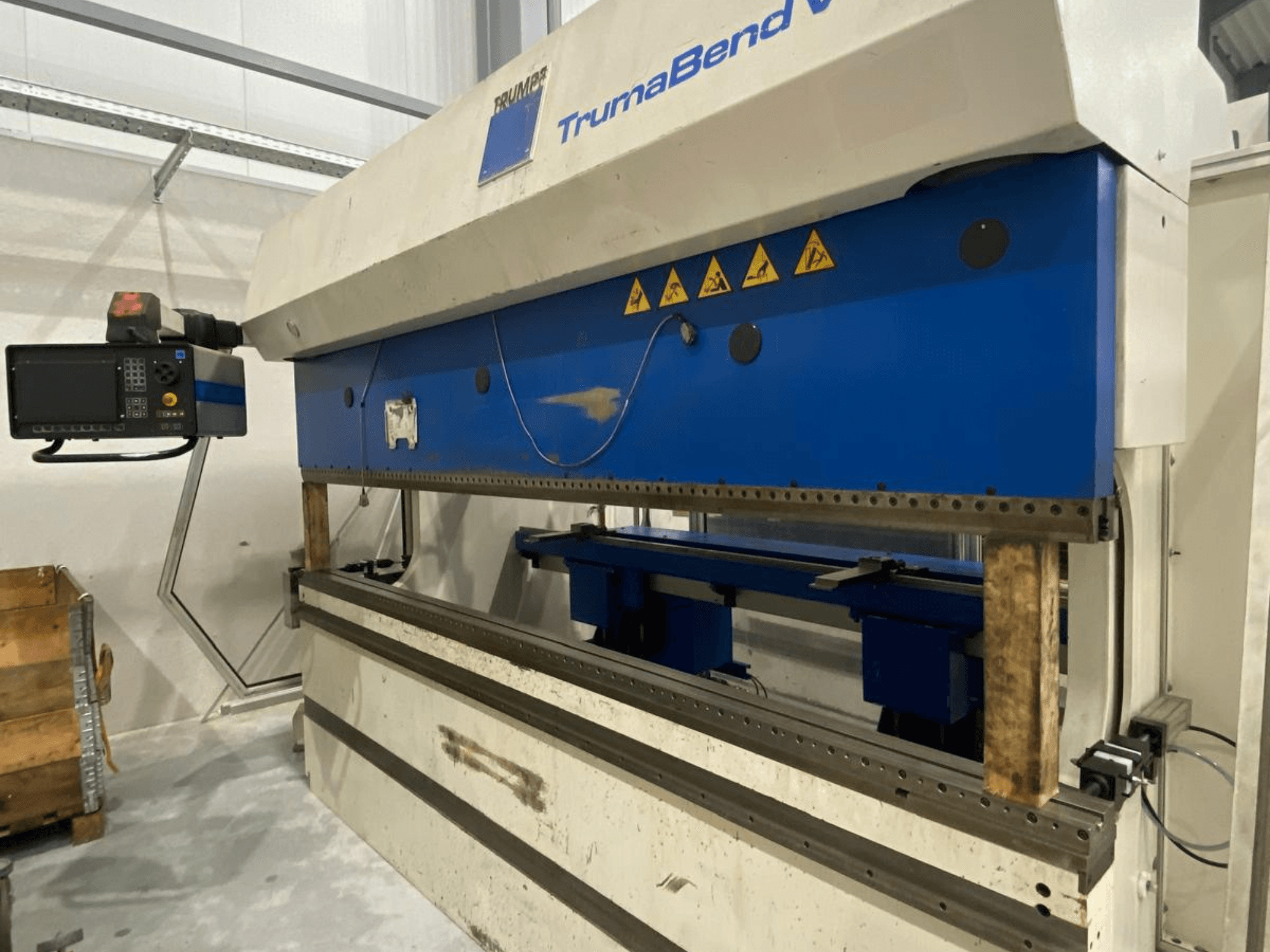 Plegadora TRUMPF Trumabend V130, vista frontal, con el panel de control, los elementos azules y las etiquetas de advertencia de seguridad visibles.