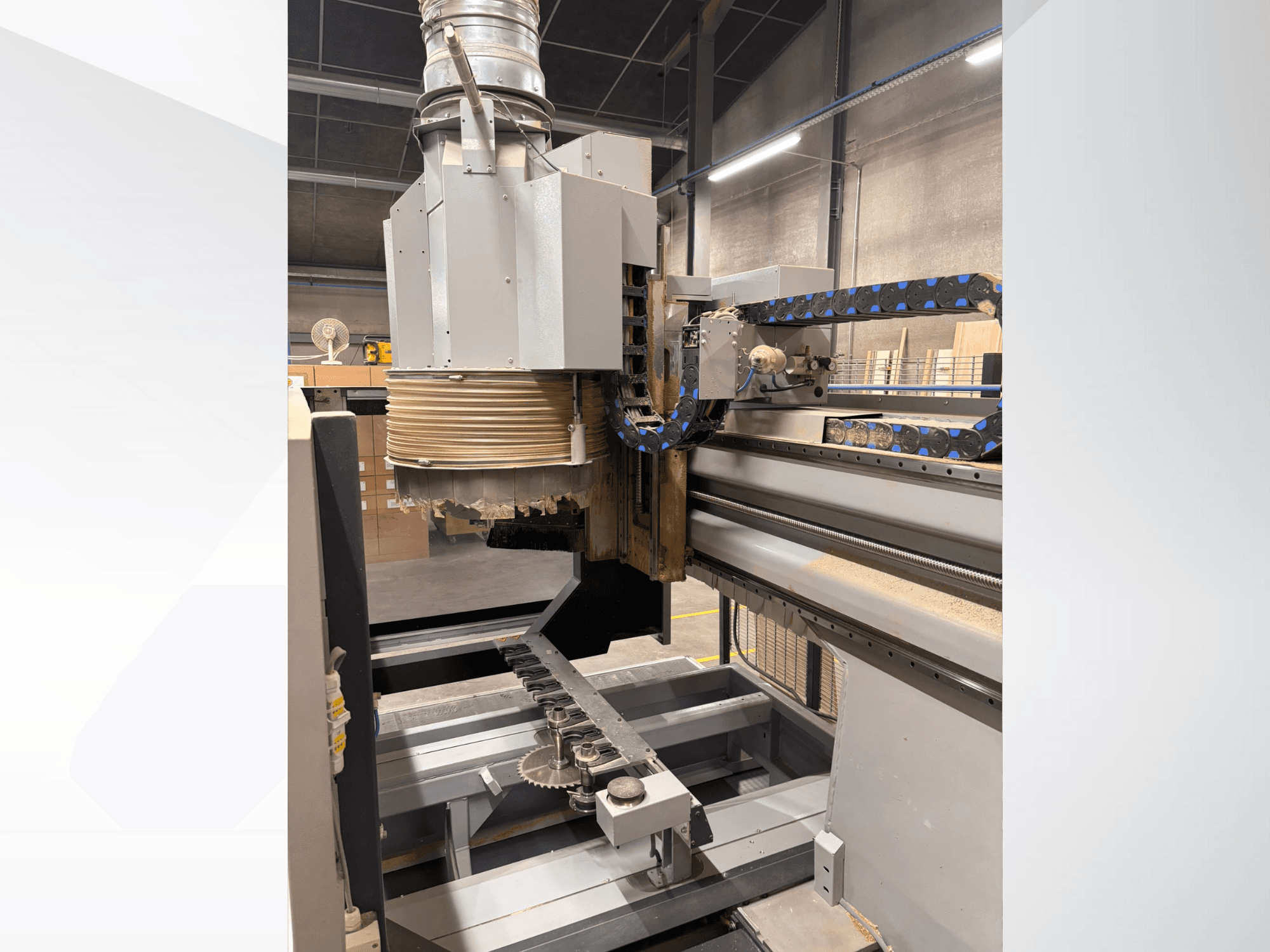 Máquina fresadora CNC con un gran husillo y cinta transportadora, vista lateral, mostrando herramientas de corte de madera y componentes de maquinaria.