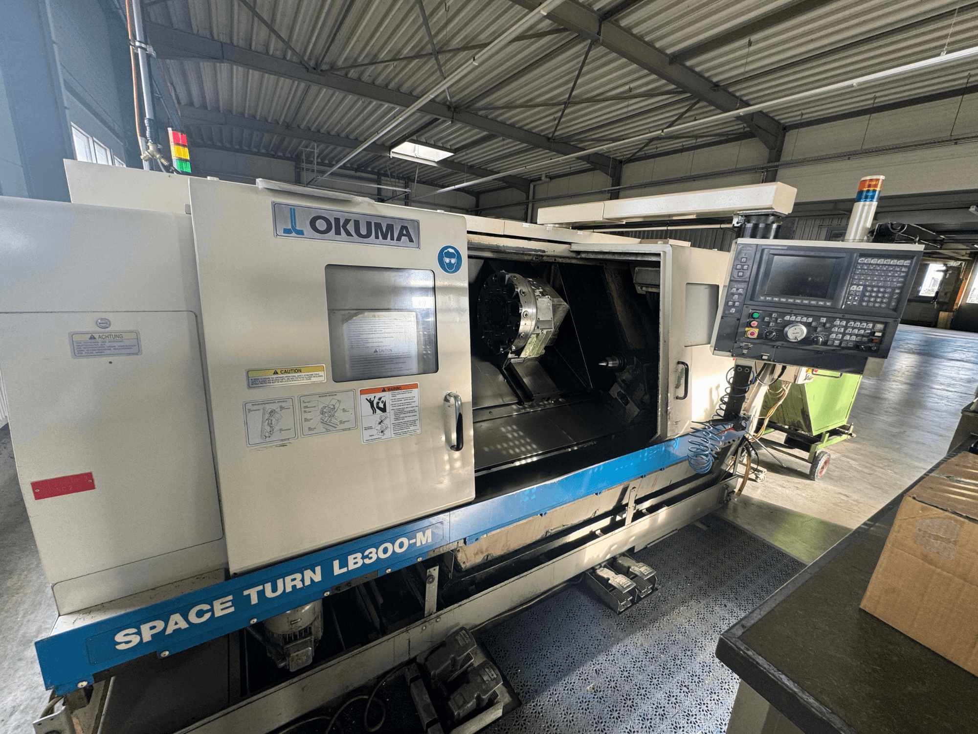 Torno CNC Okuma Space Turn LB300-M en vista frontal, con panel de control y puerta abierta que revela el área de mecanizado interior.
