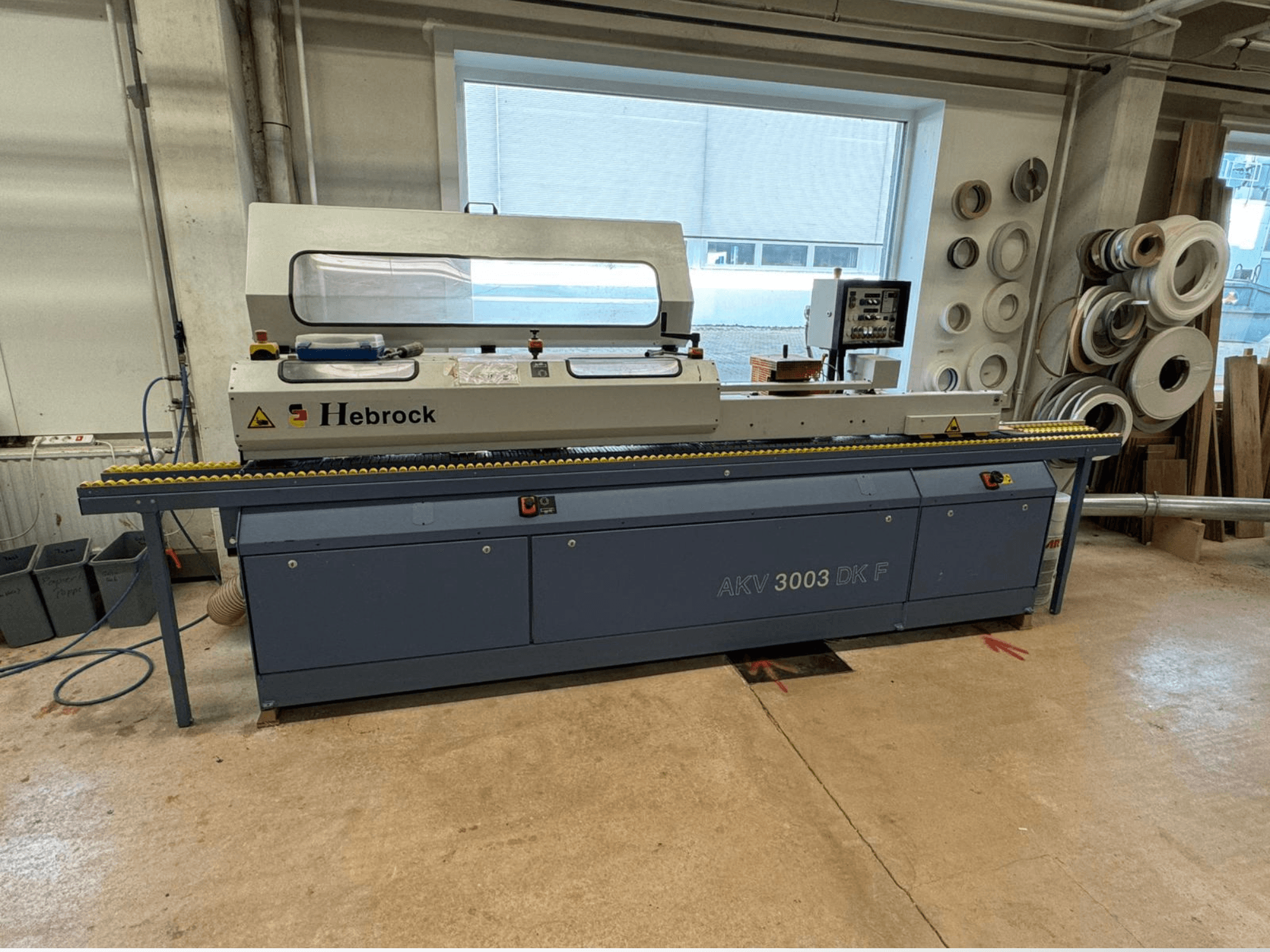 Encoladora de cantos Hebrock AKV 3003 DK F, vista frontal, con cinta transportadora y panel de control, situada en un taller.