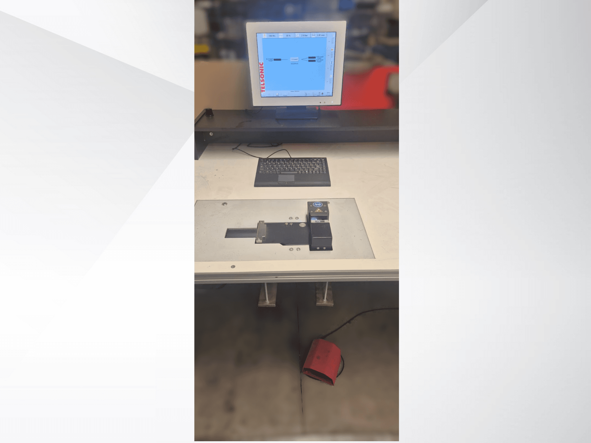 Vista desde arriba de un puesto de pruebas con un monitor de ordenador, un teclado y un panel de control con un botón y una luz verde.