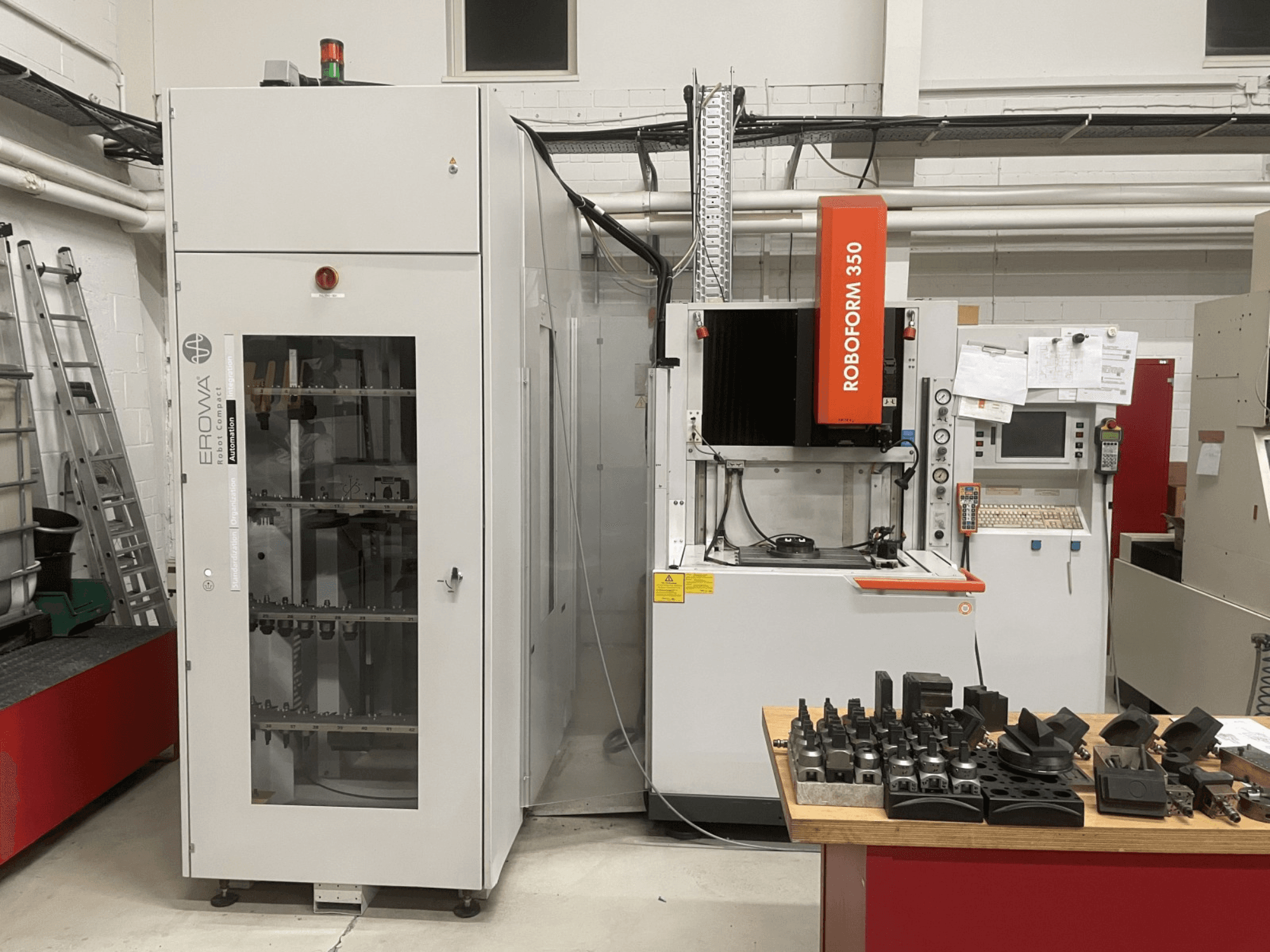 Máquina de electroerosión por penetración CHARMILLES Roboform 350, vista frontal, con herramientas expuestas sobre una mesa y equipos adyacentes.