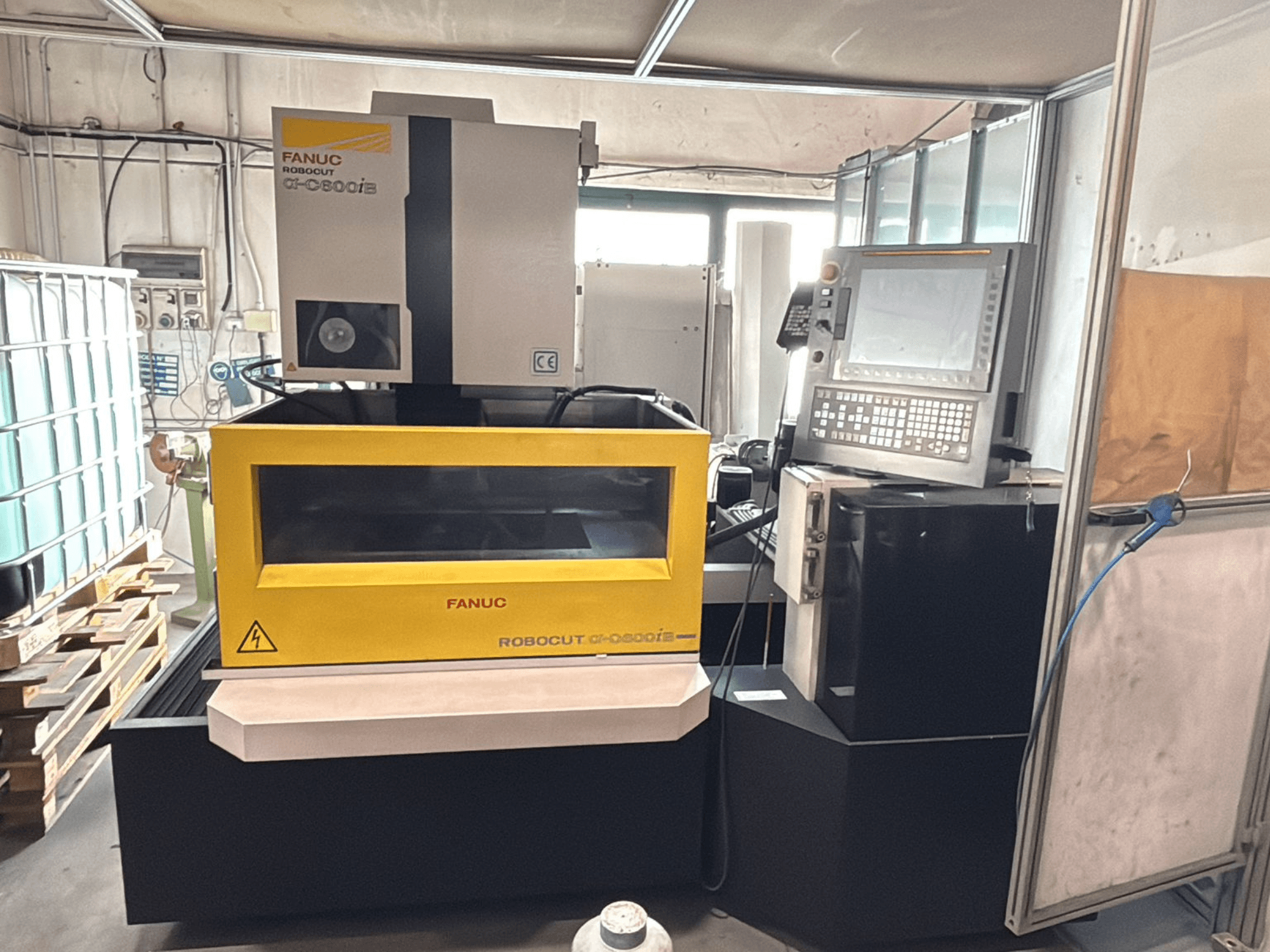 Vista frontal de una máquina CNC FANUC Robocut α-0iE con carcasa amarilla, que muestra el panel de control y la pantalla.