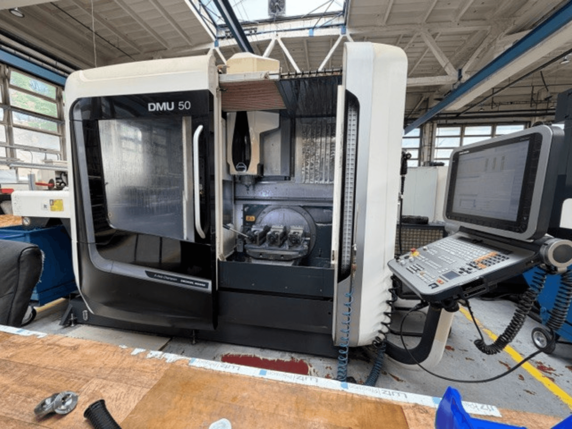 Centro de mecanizado vertical DMG MORI DMU 50 de tercera generación, visto desde delante, con la puerta abierta, el panel de control CNC a la vista y el espacio de trabajo en el interior.