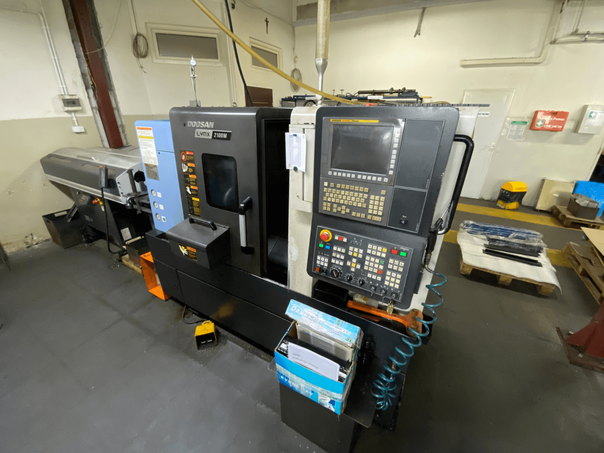 Torno horizontal DOOSAN LYNX 2100MA visto desde un lado, en el que se aprecian el panel de control, las herramientas y la zona de trabajo.
