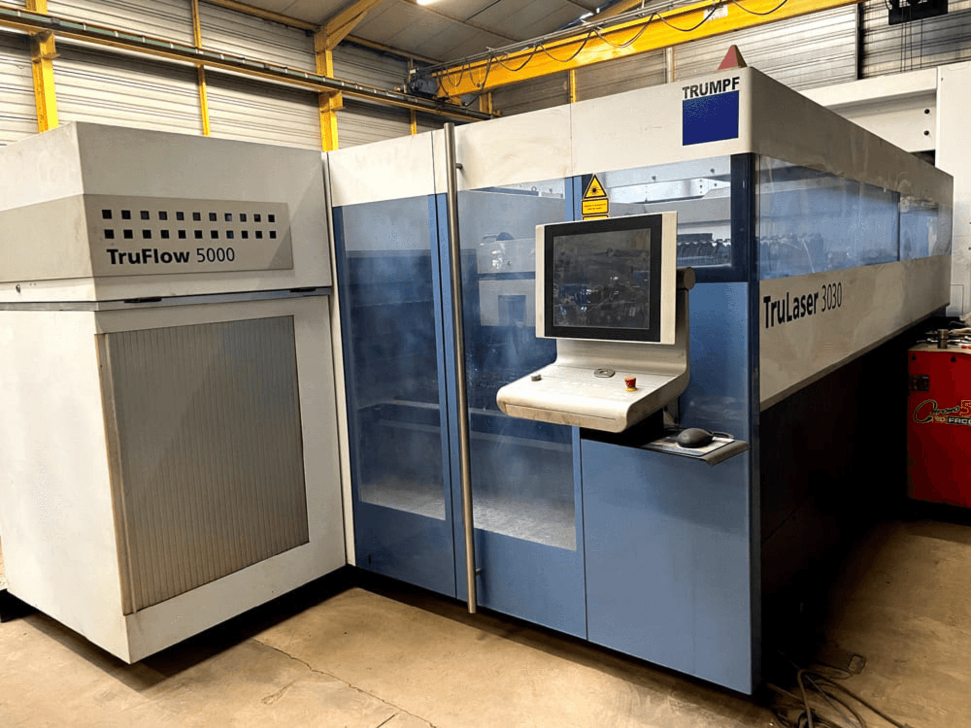 Máquina de corte por láser de CO₂ TRUMPF TruLaser 3030 vista de frente, con un panel de control y la unidad TruFlow 5000 situada junto a ella.