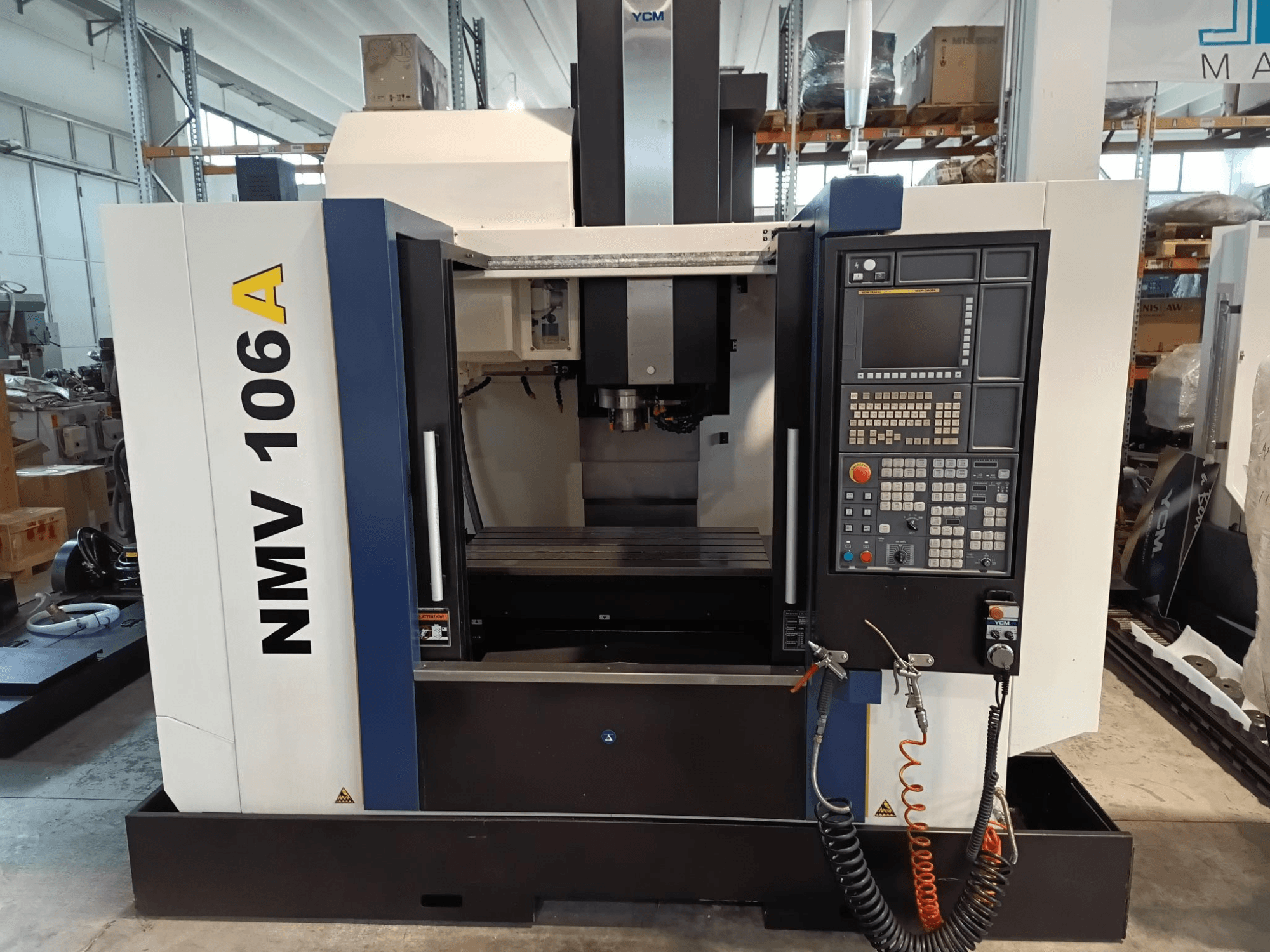 Centro de mecanizado YCM NMV 106A, vista frontal, con panel de control con botones y mangueras de refrigerante.