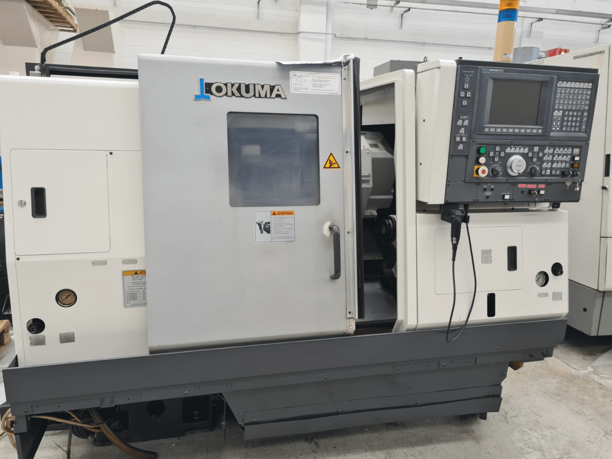 Tornos horizontales Okuma LB 300M X 500 en vista lateral, mostrando el panel de control, el acceso al husillo y las advertencias de seguridad.