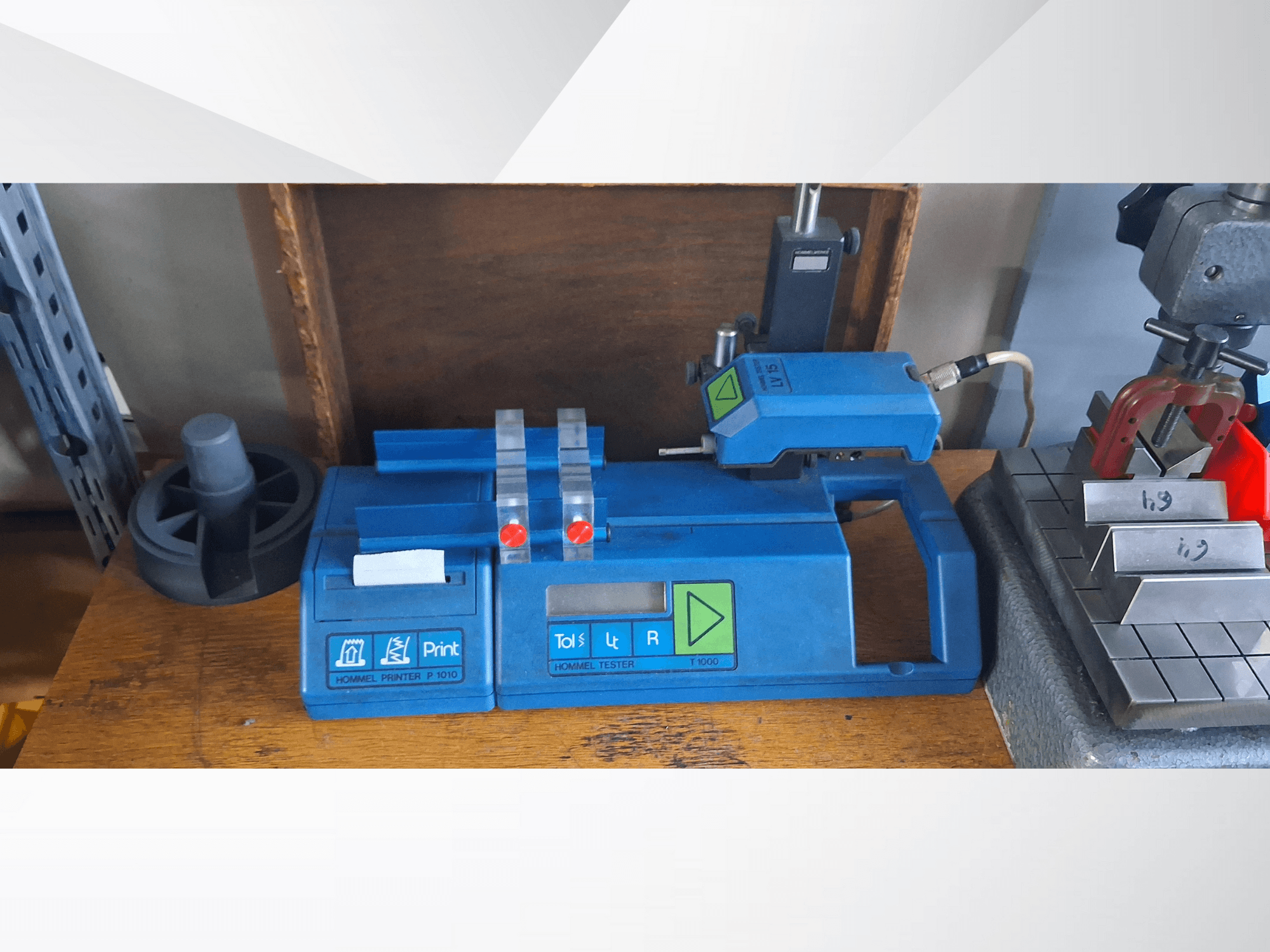 Impresora Hommel P 1010 y Tester T1000 en vista lateral, con carcasa azul, botones e indicadores rojos, sobre un banco de trabajo.