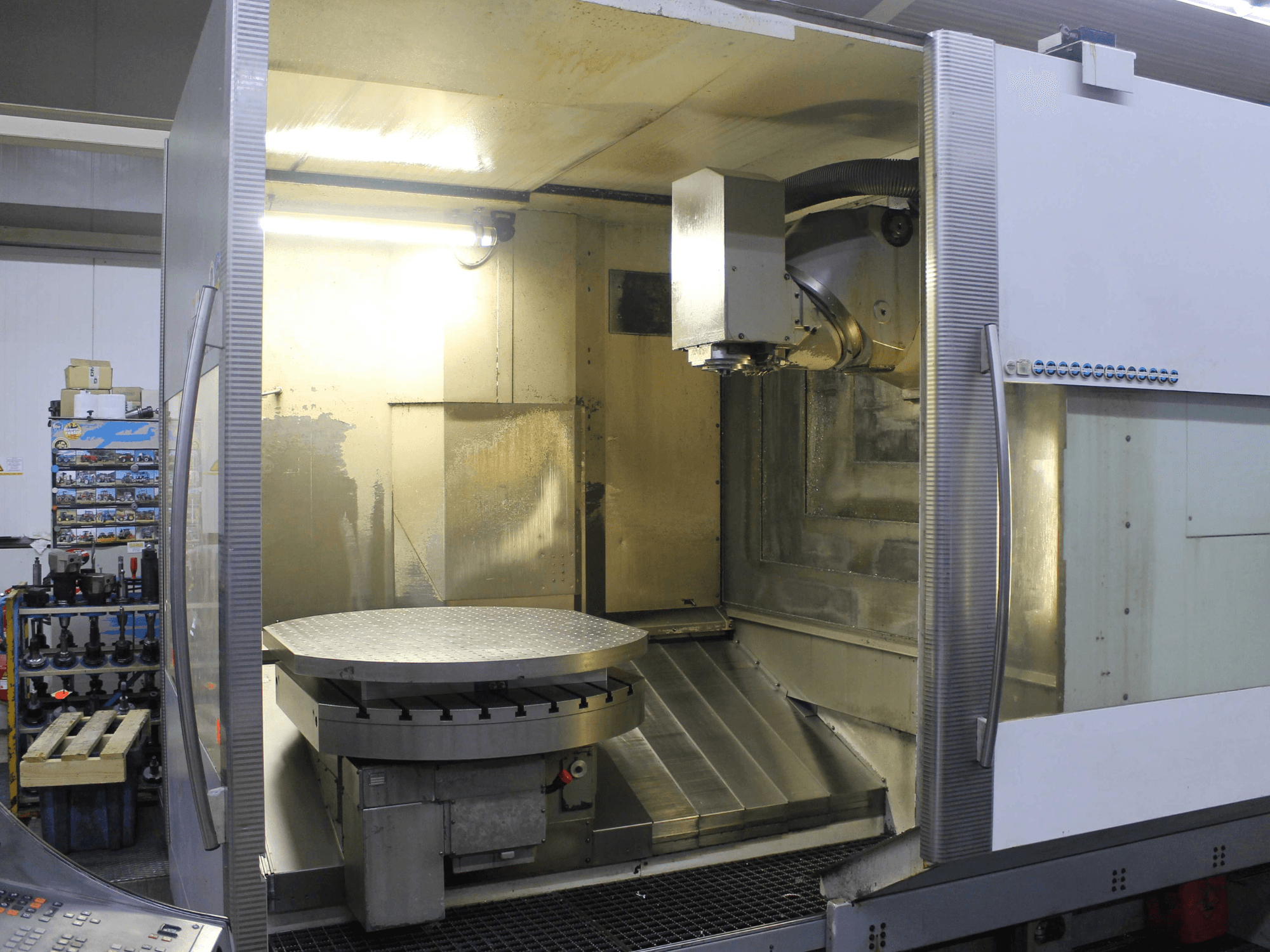Fresadora CNC con mesa giratoria circular y cabezal de corte, mostrada desde una vista frontal, con superficies metálicas e iluminación.