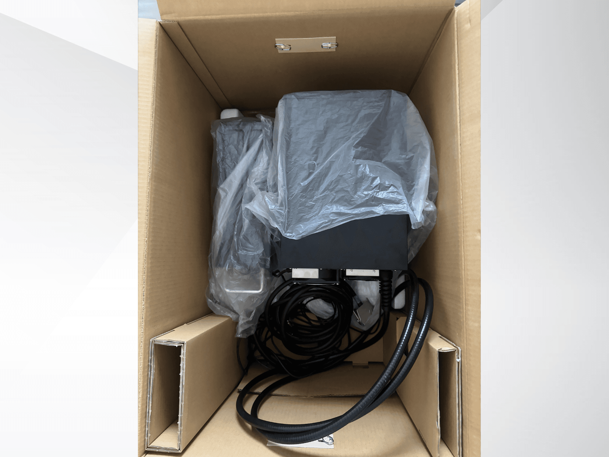 Máquina de marcado láser KEYENCE MD-X2500A en una caja de cartón, parcialmente cubierta con plástico, en la que se ven los cables y los componentes.
