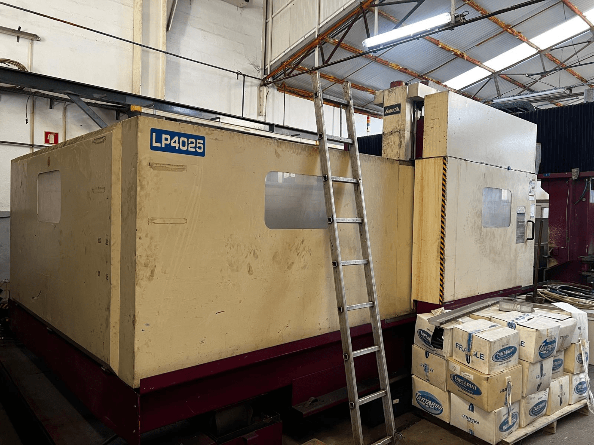 Fresadora de pórtico AWEA LP4025 en un entorno industrial; vista lateral en la que se aprecian la maquinaria de gran tamaño y las cajas de almacenamiento.