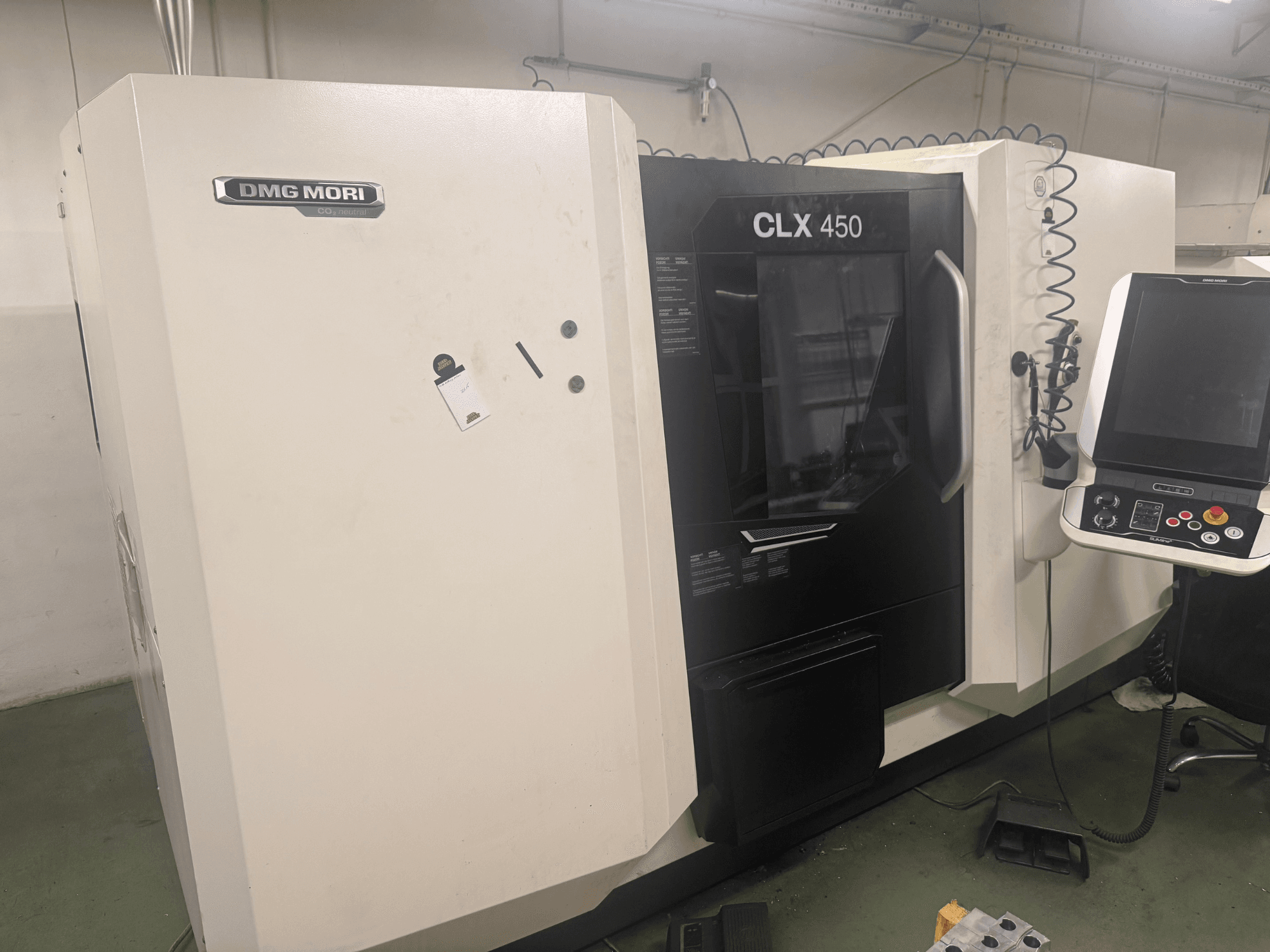 Máquina CNC DMG MORI CLX 450, vista lateral con panel de control, botones operativos visibles y espacio de trabajo limpio.