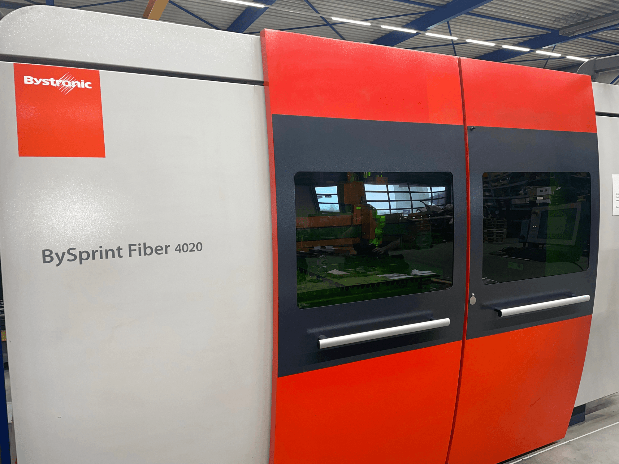 Bystronic BySprint Fiber 4020 en vista frontal, con un diseño de panel gris y rojo con grandes ventanas e interfaz de control visible en el interior.