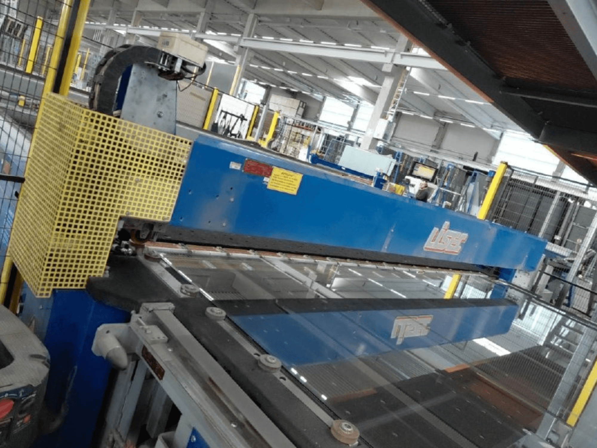 Vista frontal de la línea de corte combinada de vidrio laminado de seguridad (VSG) y vidrio flotado de LISEC, en la que se aprecian una herramienta de corte azul y una malla protectora.