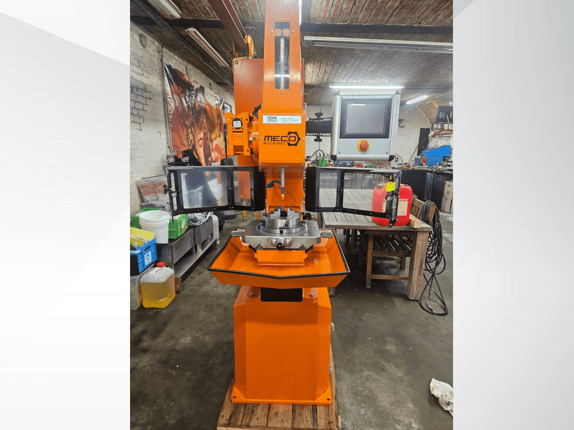 Fresadora MEC naranja, vista frontal, con panel de control y mesa de trabajo, situada en un taller con herramientas y materiales.