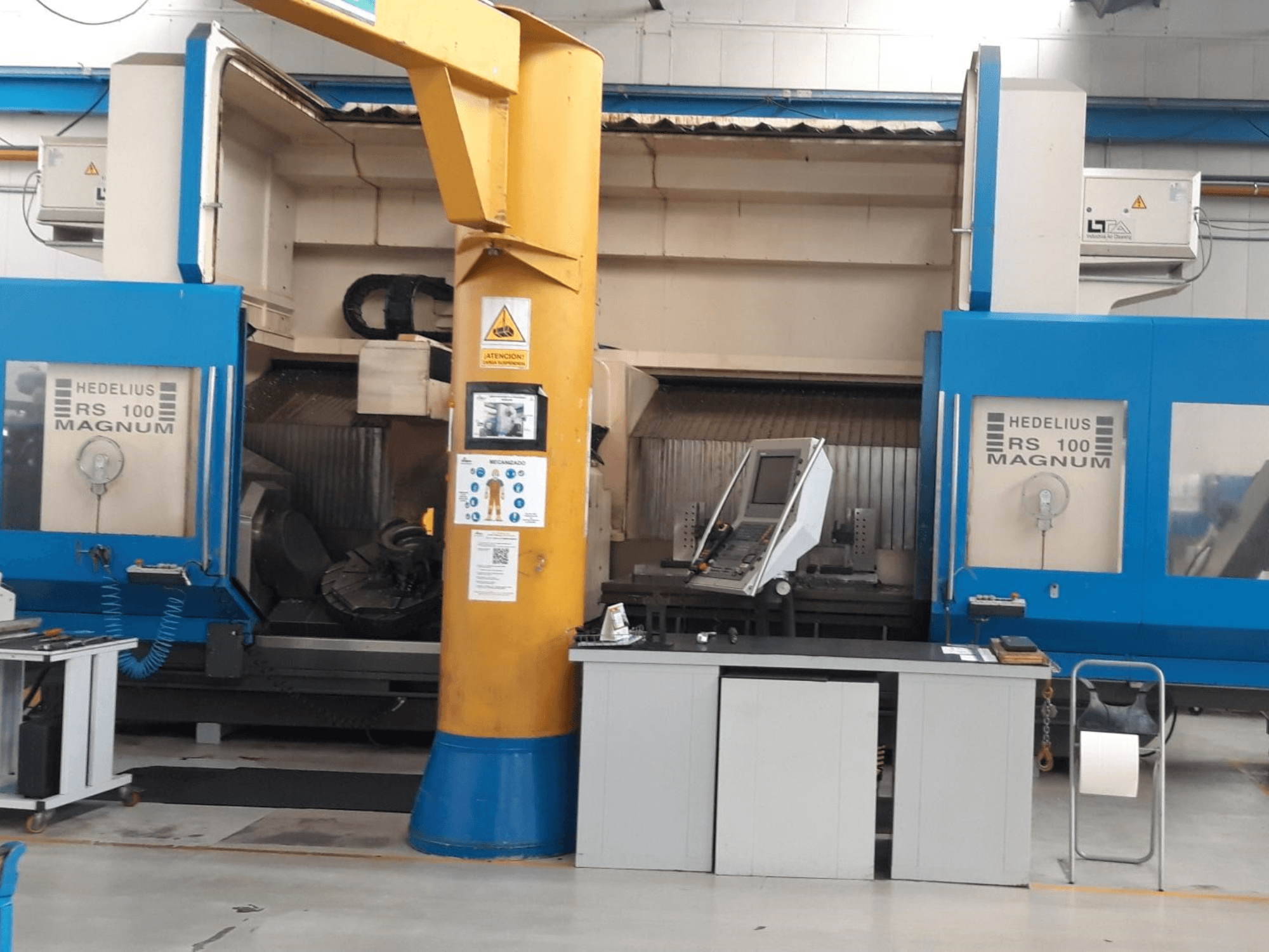 Máquina HEDALIUS RS 100 MAGNUM, vista frontal; incluye panel de control y columna de soporte amarilla, colocada en un espacio de trabajo industrial.