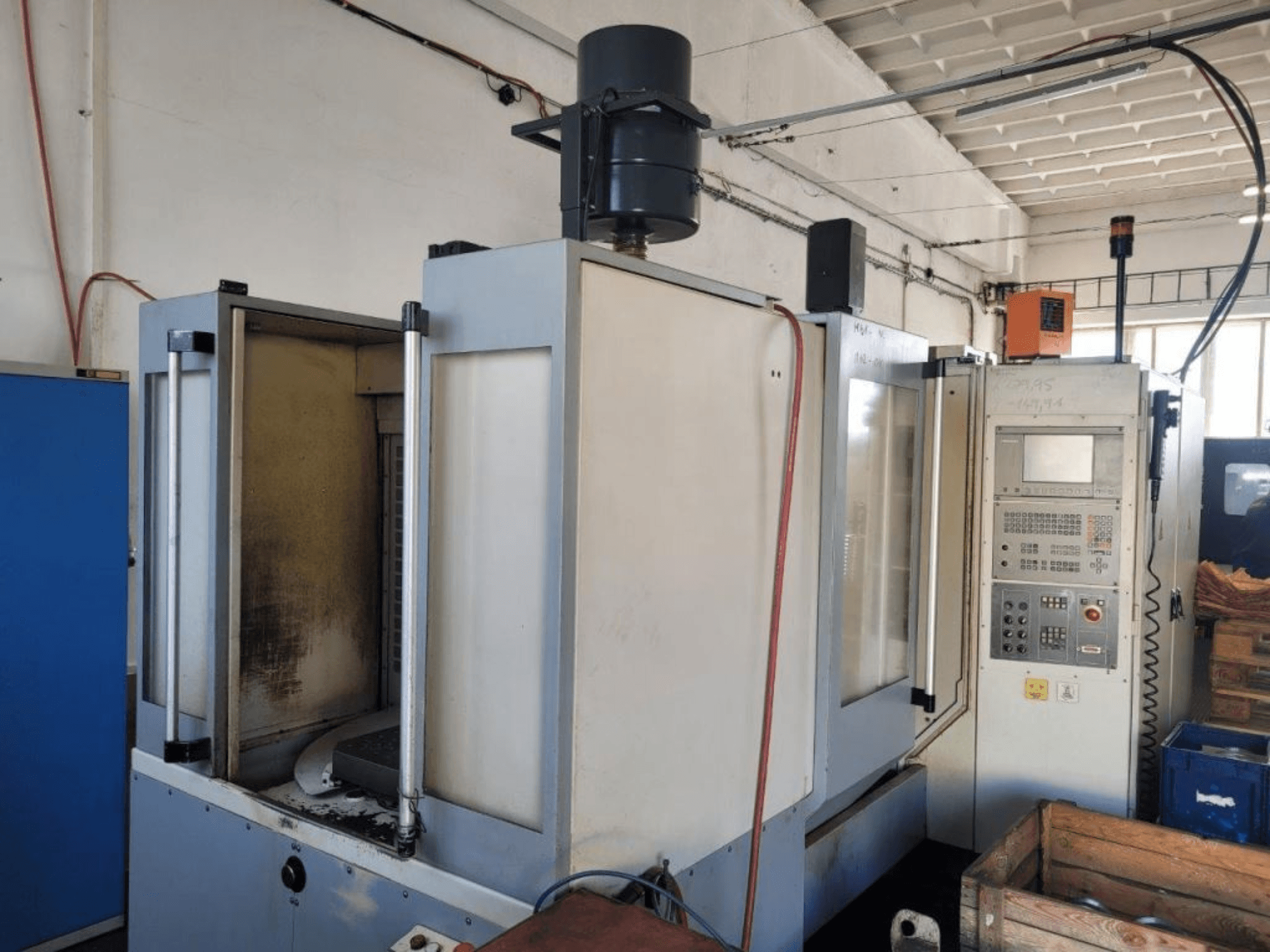 Fresadora CNC industrial con panel de control, vista lateral, mostrando la carcasa y la suciedad visible en las superficies.