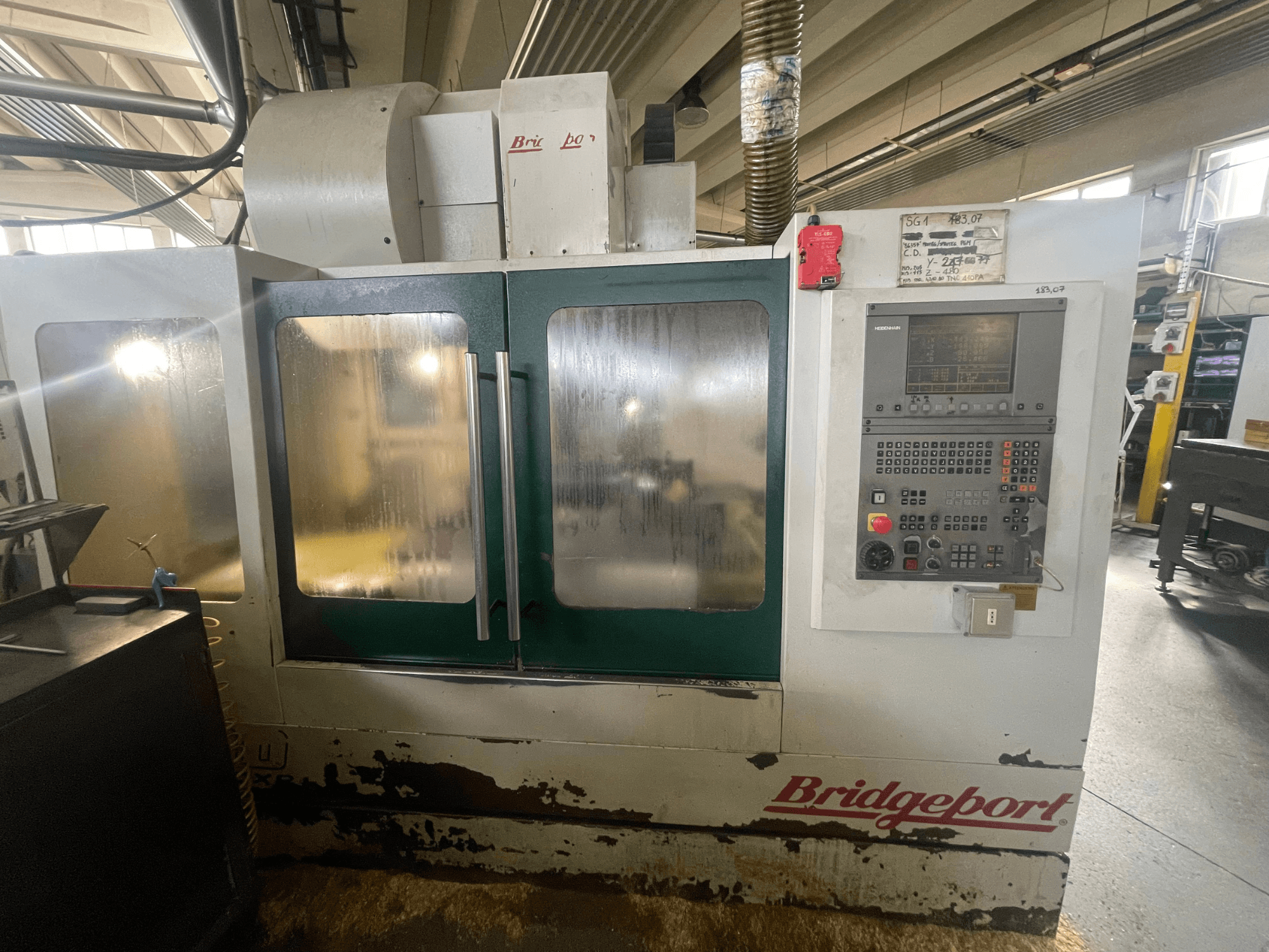 Centro de mecanizado vertical Bridgeport VMC 1000/30, vista frontal con el panel de control, en la que se aprecia el exterior desgastado y las puertas verdes.