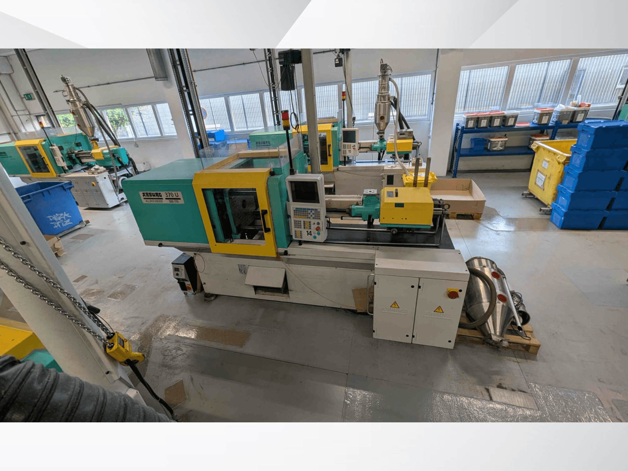Vista frontal de la máquina de moldeo por inyección vertical Arburg 370 U 500-170, con el panel de control y los componentes de la máquina, en un taller.