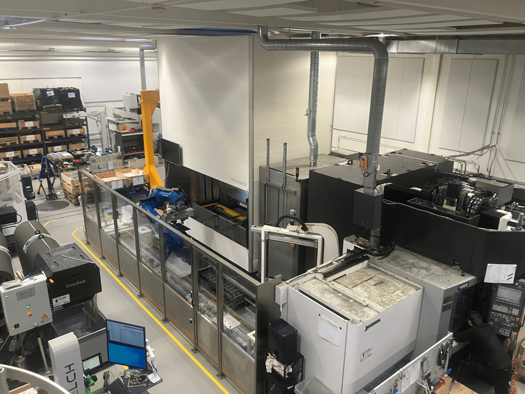 Sistema de automatización Logimat de SSI SCHAFER en un almacén, vista frontal; incluye brazo robótico, estanterías de almacenamiento y maquinaria.