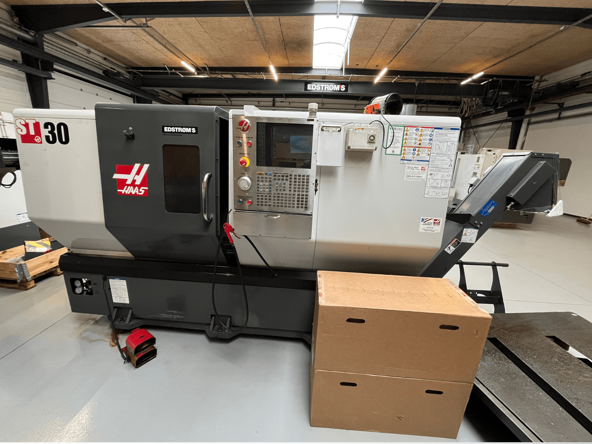 Torno CNC Haas ST-30 visto desde un lateral, con un panel de control, la placa del modelo y dos cajas de cartón cerca.