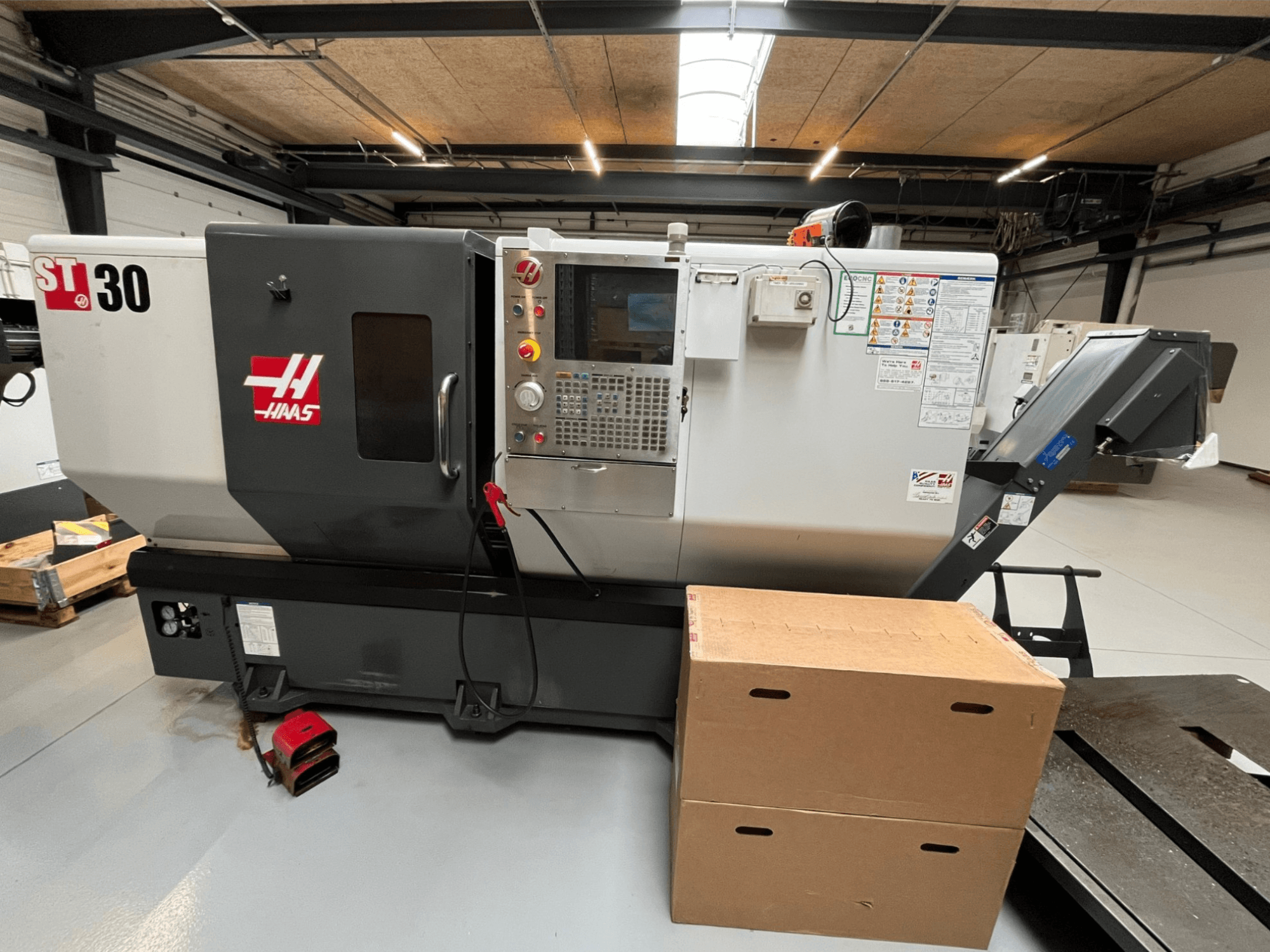 Torno CNC Haas ST-30, vista frontal, presenta panel de control con botones, parada de emergencia y dos cajas de cartón apiladas.