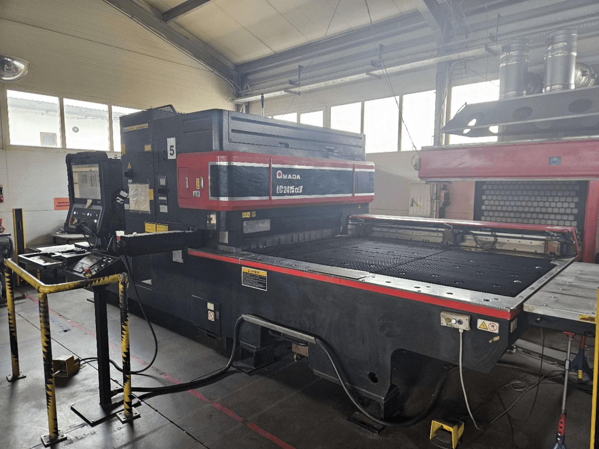 Máquina de corte por láser de CO₂ AMADA LC2415 Alpha 5, vista frontal en la que se aprecian el panel de control y la mesa de corte con las barreras de seguridad.