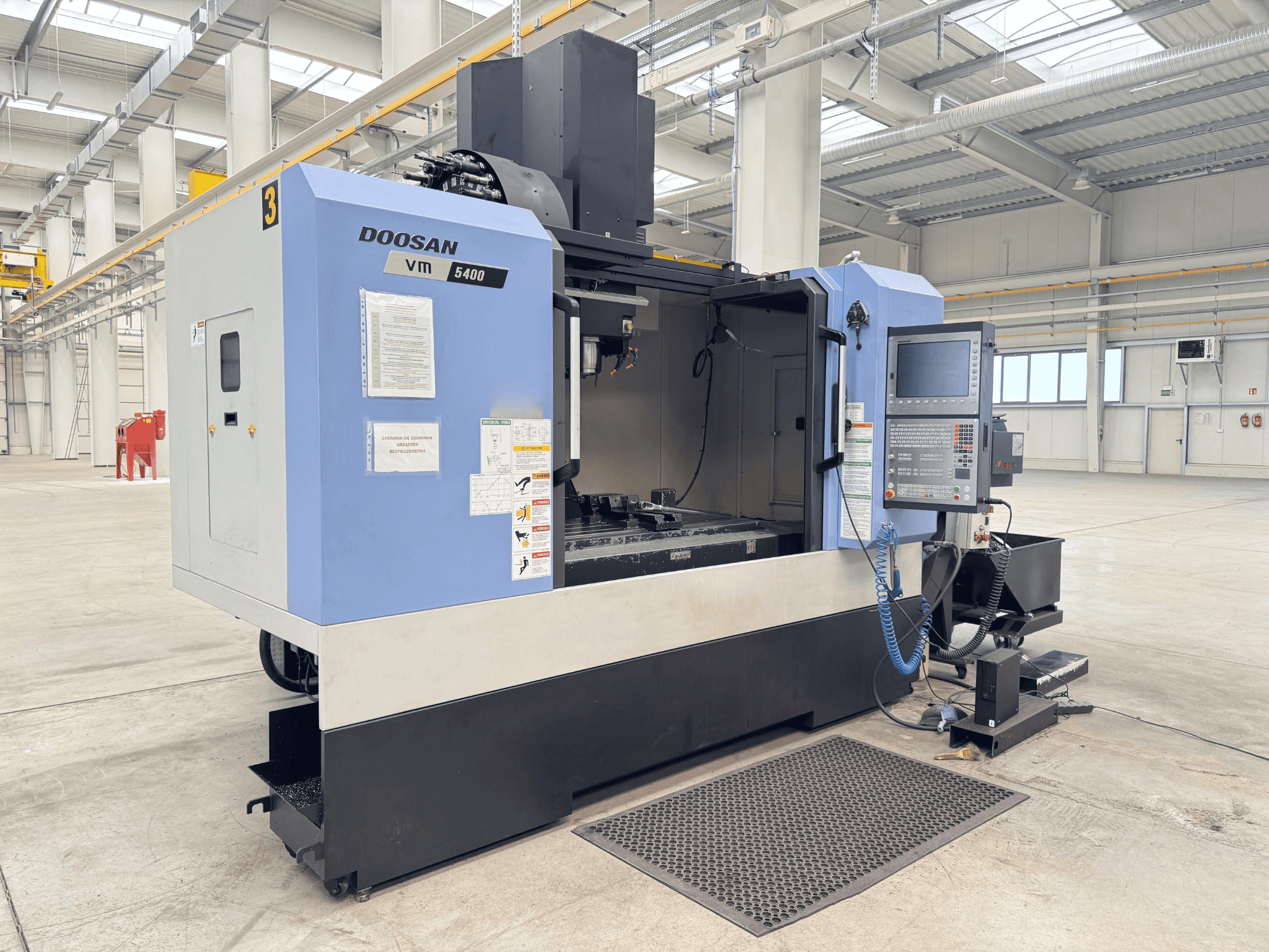Centro de mecanizado vertical DOOSAN VM 5400, vista frontal que muestra el panel de control y la zona de trabajo en un amplio entorno industrial.