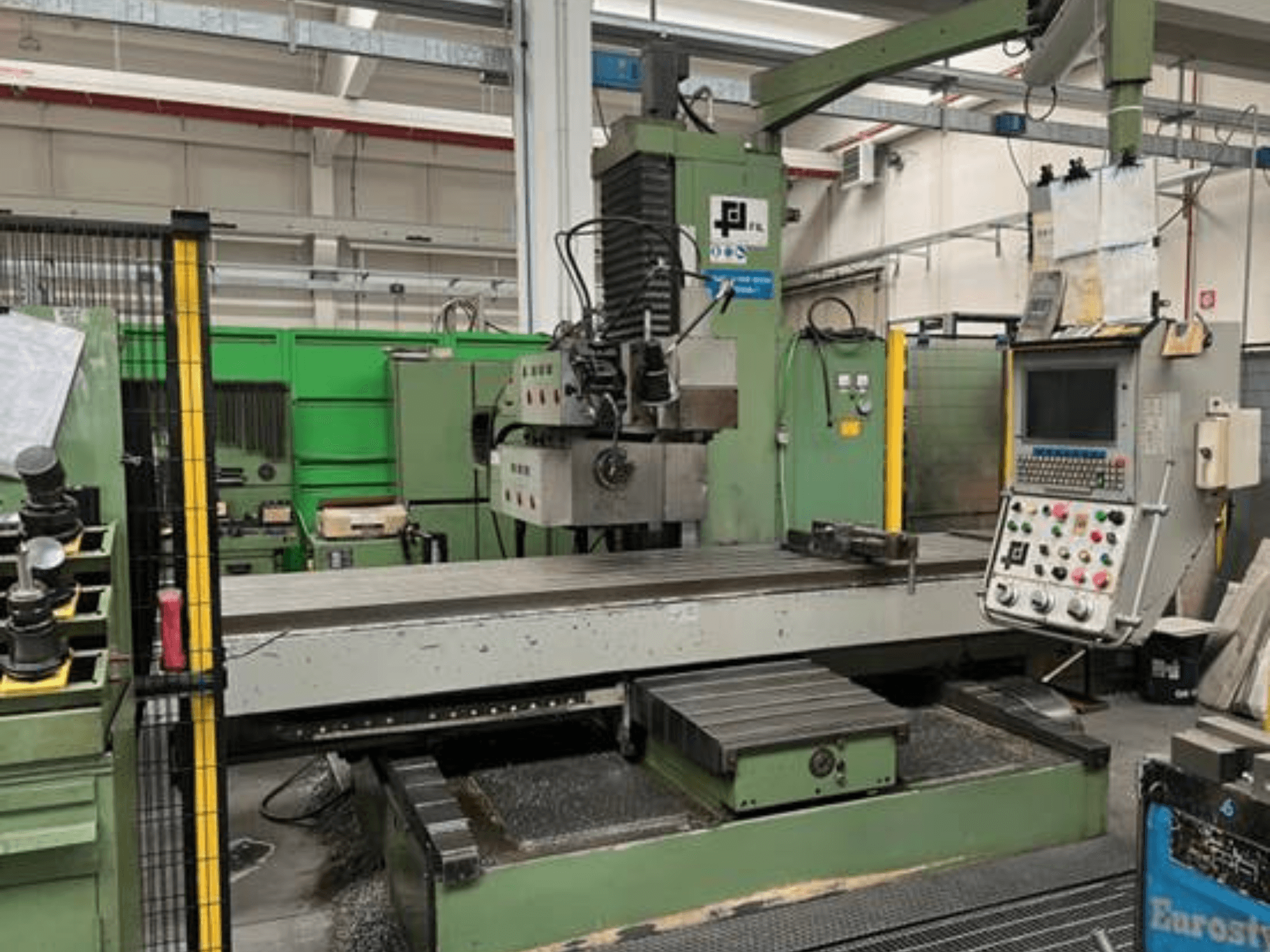 Fresadora industrial de JFL, vista frontal con panel de control, gran mesa plana y virutas de metal en el suelo.