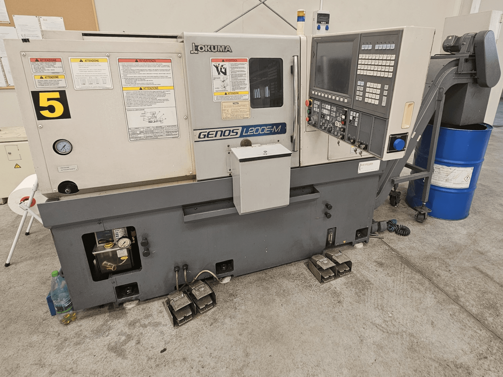 Tornos horizontales Okuma GENOS L200E-M en vista frontal, con panel de control, etiquetas y barril de refrigerante.