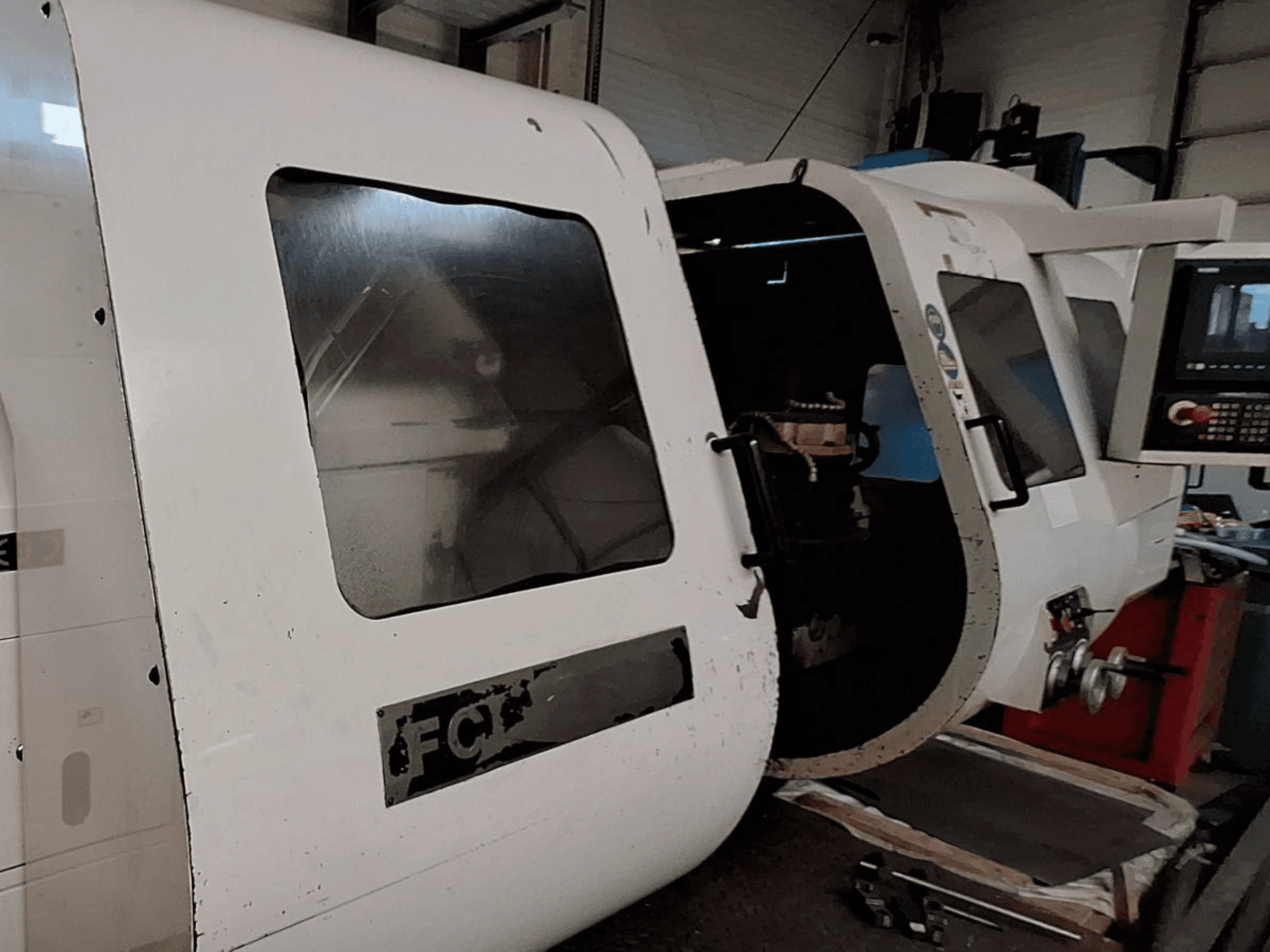 Máquina CNC blanca con panel de control visible y puerta abierta, mostrando los componentes interiores; vista frontal. Marca: FCT.