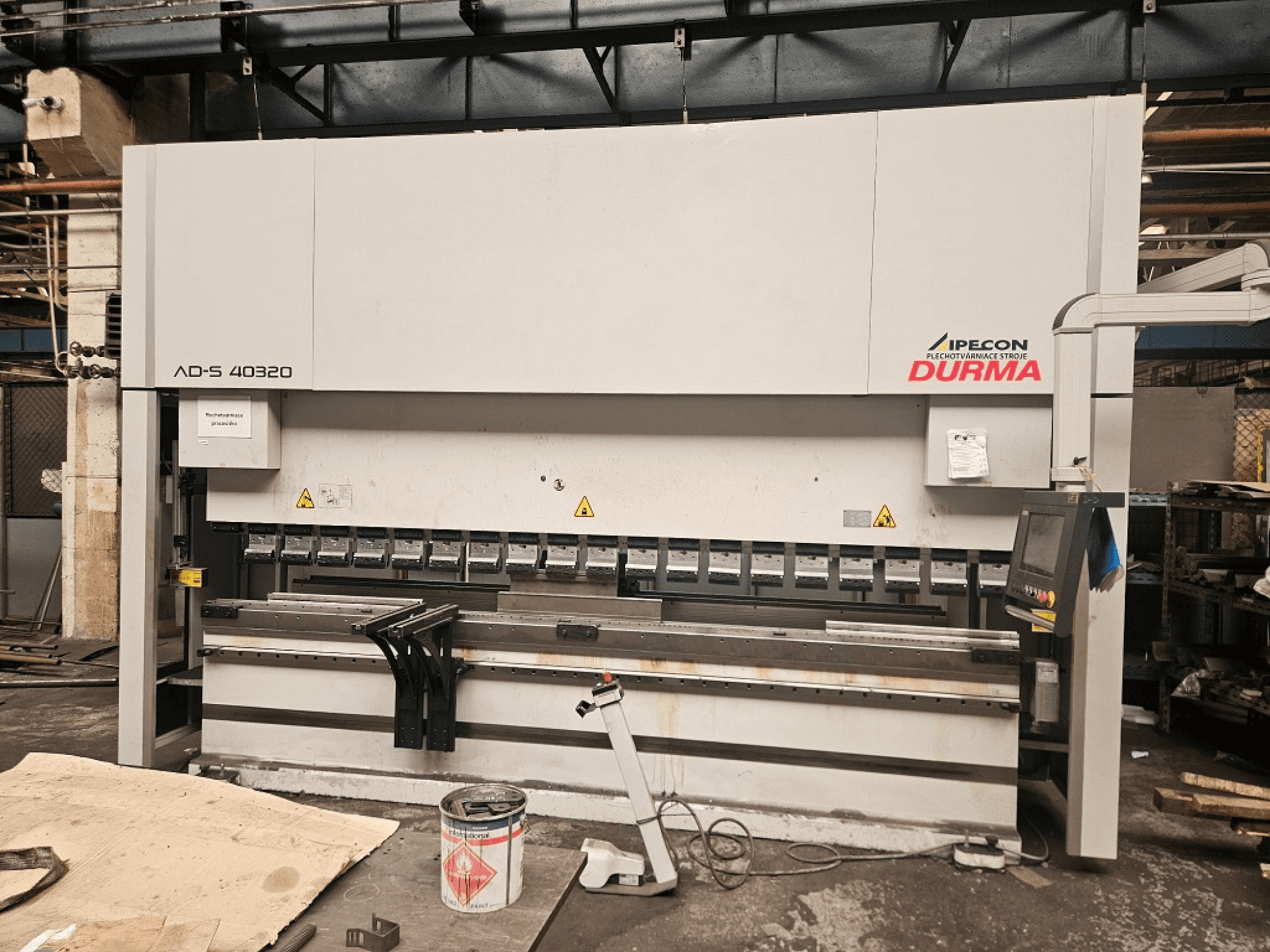 Plegadora Durma AD-S 40320 vista frontal, en la que se aprecian el panel de control, las herramientas de plegado y las advertencias de seguridad en un entorno de taller.