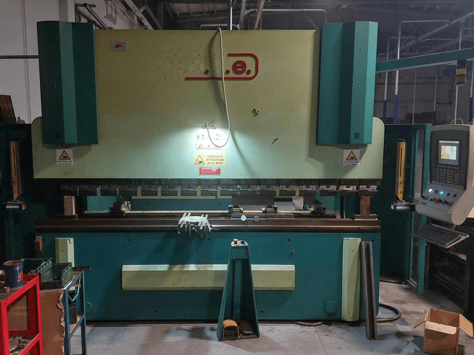 Vista frontal de la prensa plegadora Gade PS-C 3120, en la que se aprecian el panel de control, las señales de seguridad y la zona de trabajo con herramientas y materiales.