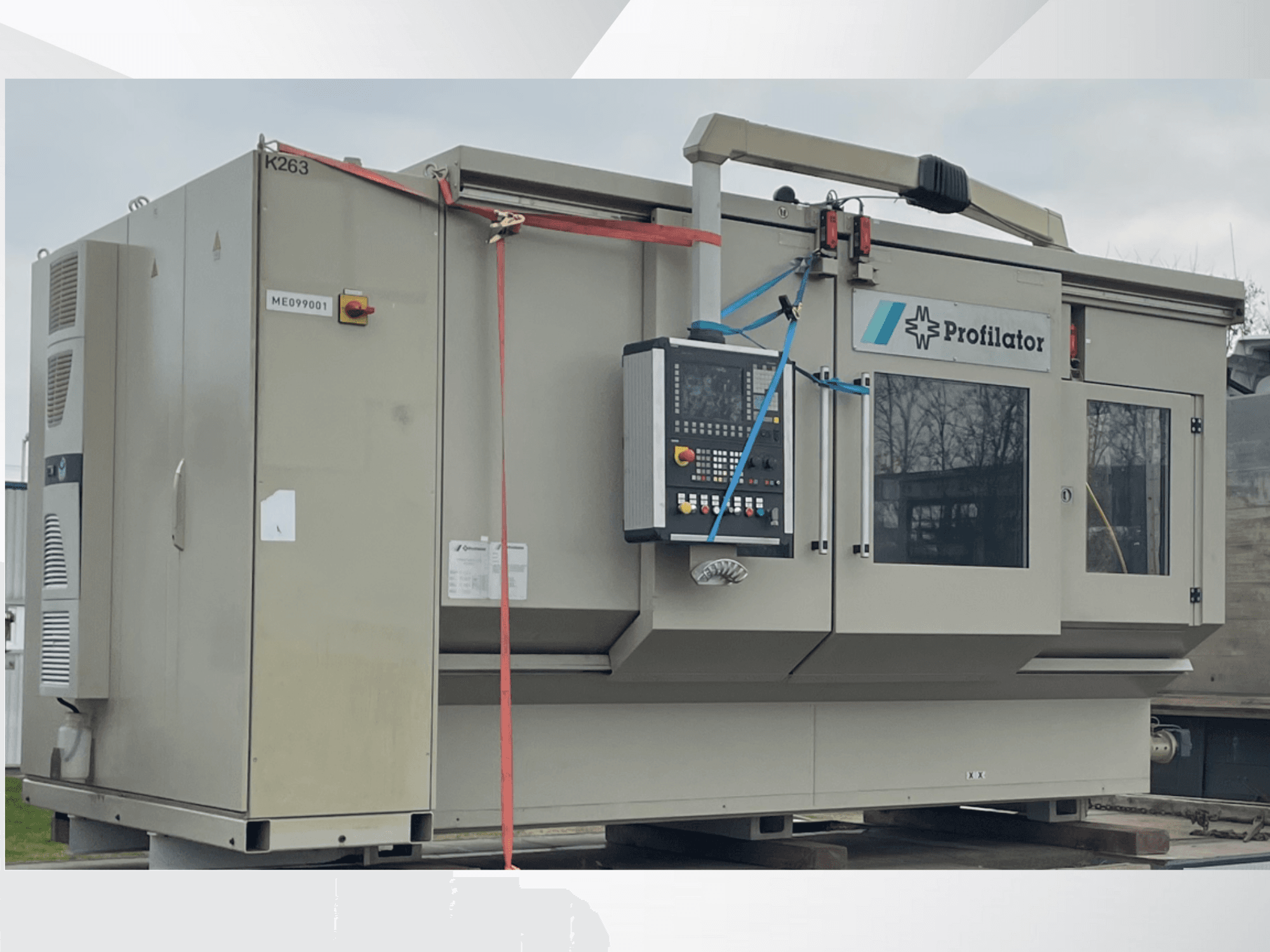 Máquina perfiladora en vista lateral, con panel de control, etiquetas de seguridad y flejes de protección, sobre una plataforma de madera.