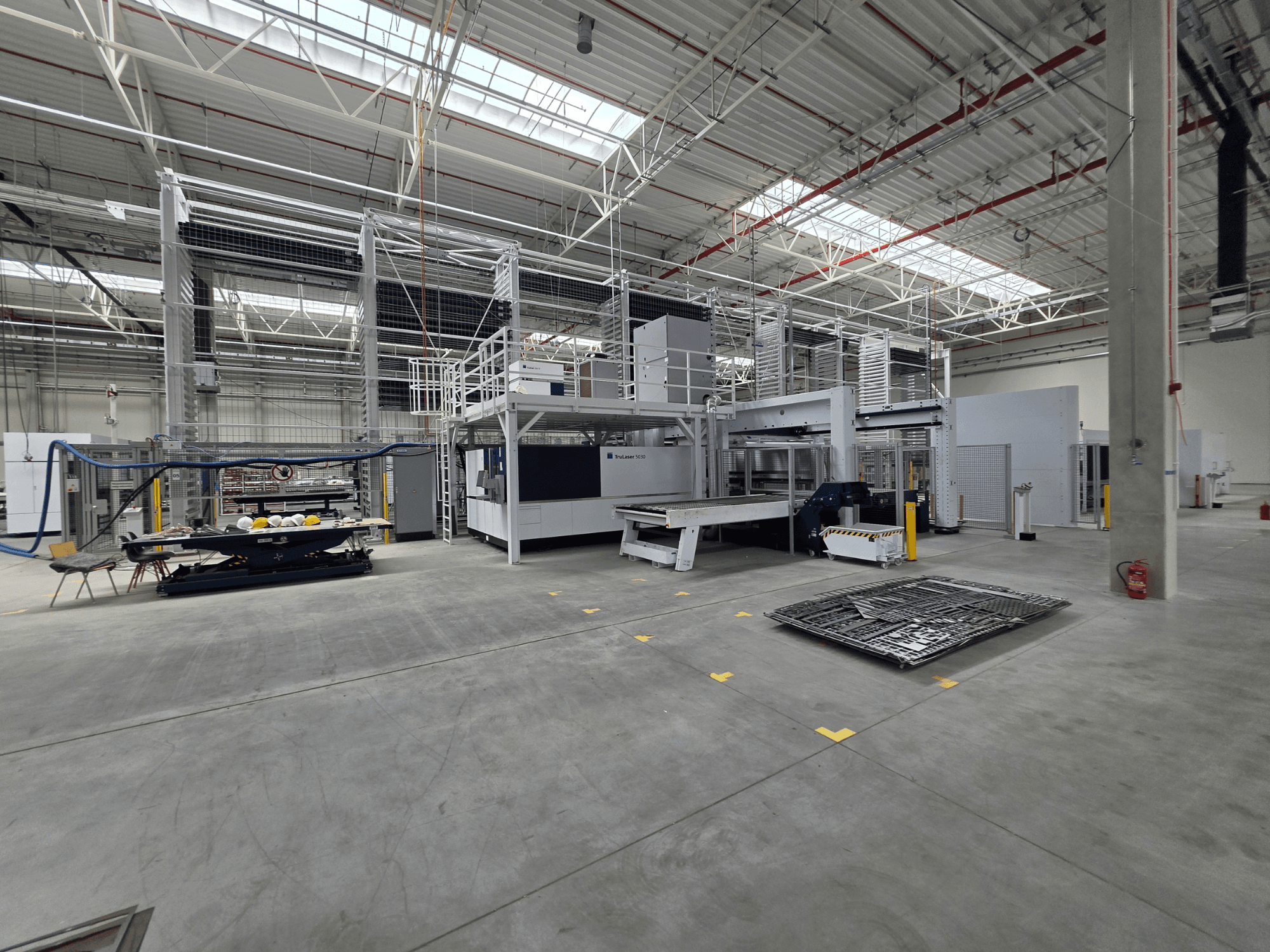 Sistema automatizado de producción de chapa de TRUMPF; vista lateral en la que se aprecian la maquinaria, el espacio de trabajo y las herramientas en un gran entorno industrial.