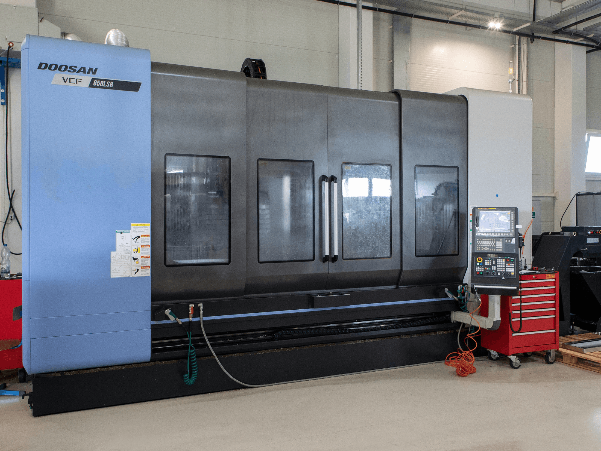 Centro de fresado y torneado DOOSAN VCF850, vista frontal; cuenta con dos grandes ventanas, un panel de control y un compartimento para herramientas. Ideal para el mecanizado.