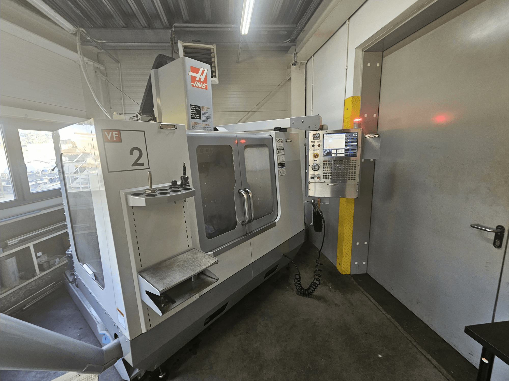 Fresadora CNC Haas VF-2, vista frontal, mostrando el panel de control, los portaherramientas y una ventana transparente en el espacio de trabajo.