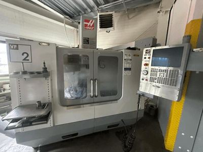 Máquina CNC Haas VF-2, vista frontal, con controles, portaherramientas y puertas transparentes con herramientas visibles en el interior del armario.
