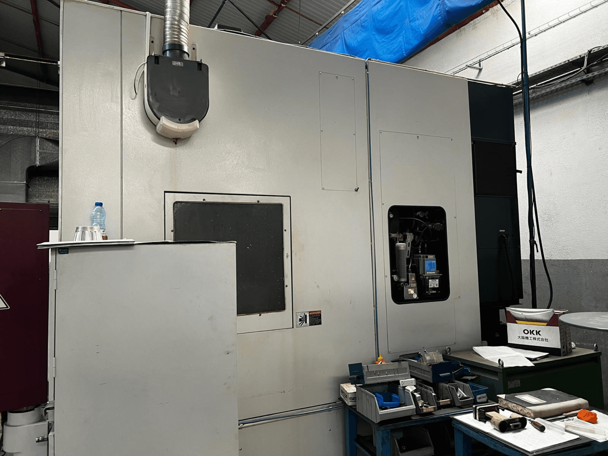 Centro de mecanizado vertical OKK VP600 en un taller; vista lateral en la que se aprecian los detalles de la máquina y las herramientas sobre una mesa cercana.