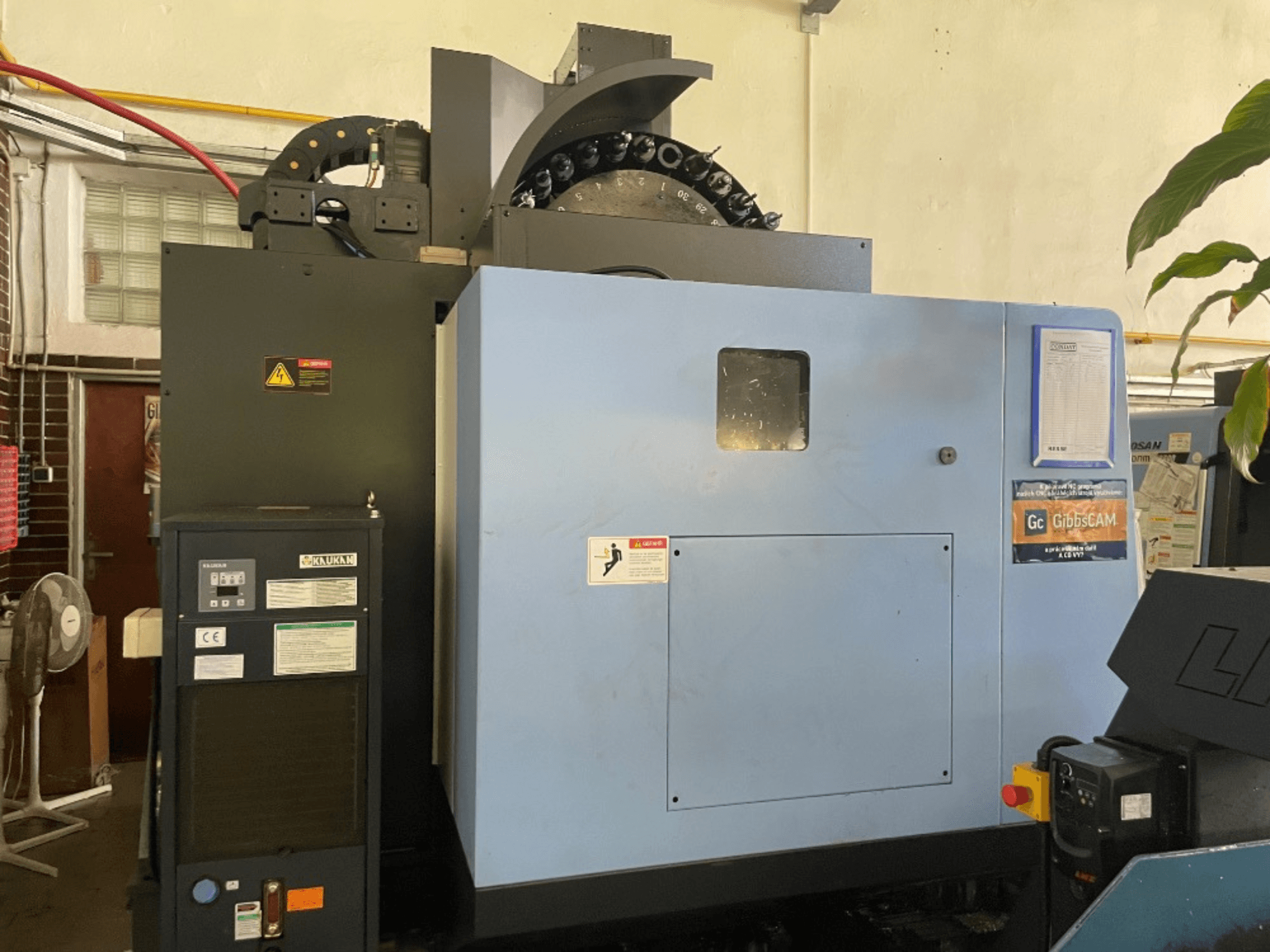 Vista frontal de un centro de mecanizado vertical DOOSAN DNM 5700, mostrando el panel de control, las etiquetas de seguridad y las características de la máquina.