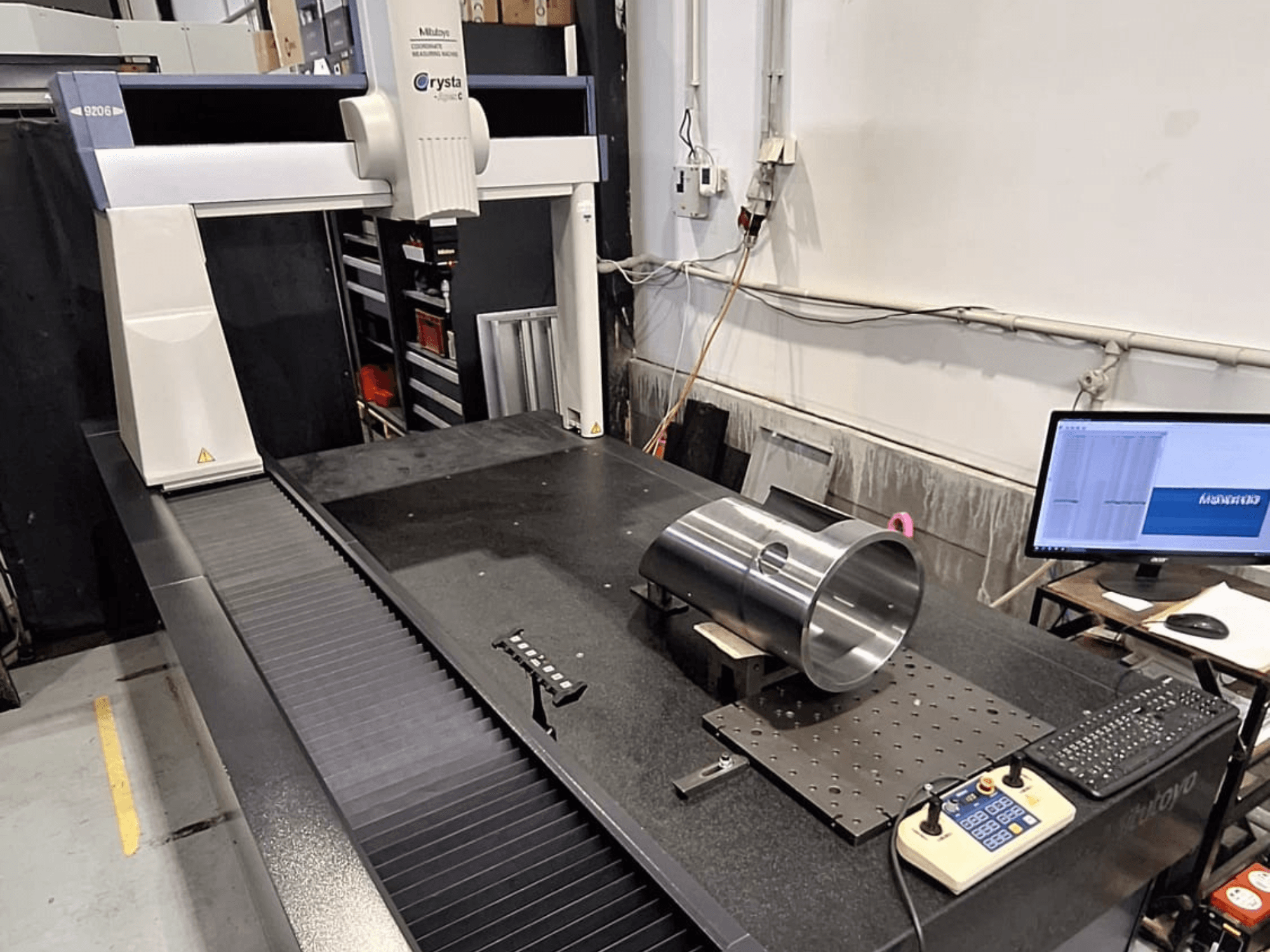 MMC Mitutoyo Crysta-Apex C9206 en vista frontal, midiendo una pieza metálica cilíndrica en una placa de superficie de granito negro.