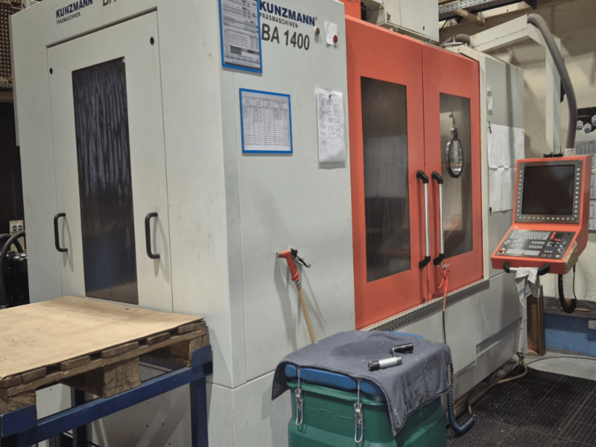 Vista frontal del Centro de Mecanizado Vertical KUNZMANN BA1400, con puertas naranjas, panel de control y mesa de trabajo.