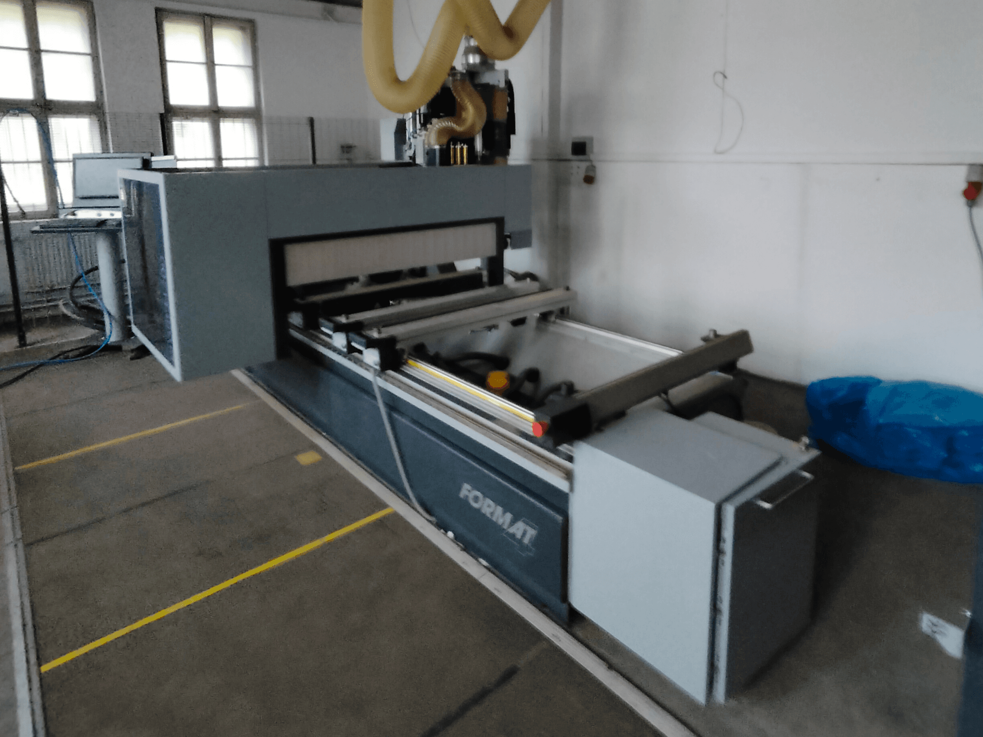 Vista frontal de una máquina CNC Format de cuerpo gris, con carriles guía y panel de control visible.