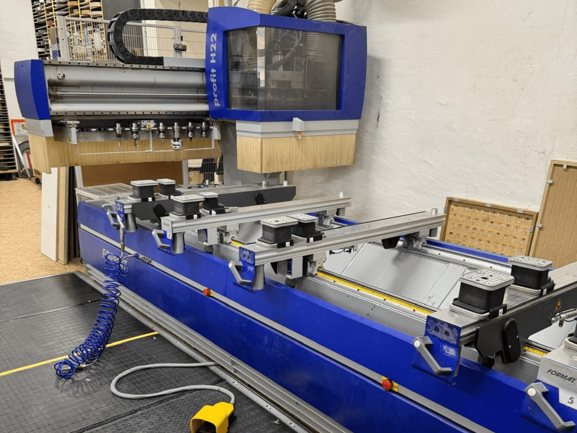 Centro de mecanizado de madera CNC FORMAT4 PROFIT H22, vista frontal, con las herramientas de mecanizado y las abrazaderas de sujeción visibles sobre el cuerpo azul.