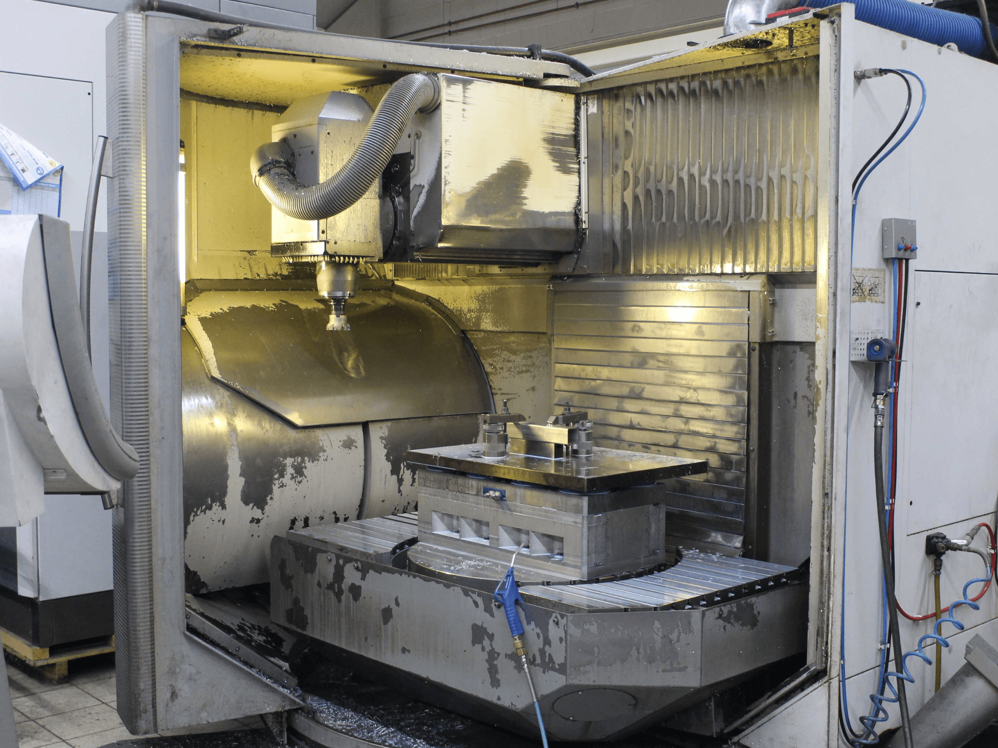 Interior de fresadora CNC, vista lateral, mostrando la pieza de trabajo y la herramienta de corte con virutas de metal y residuos de refrigerante.